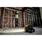 A construction worker in protective clothing is working with a drilling tool on a wooden wall in an unfinished building. A construction site lamp lies in the foreground.