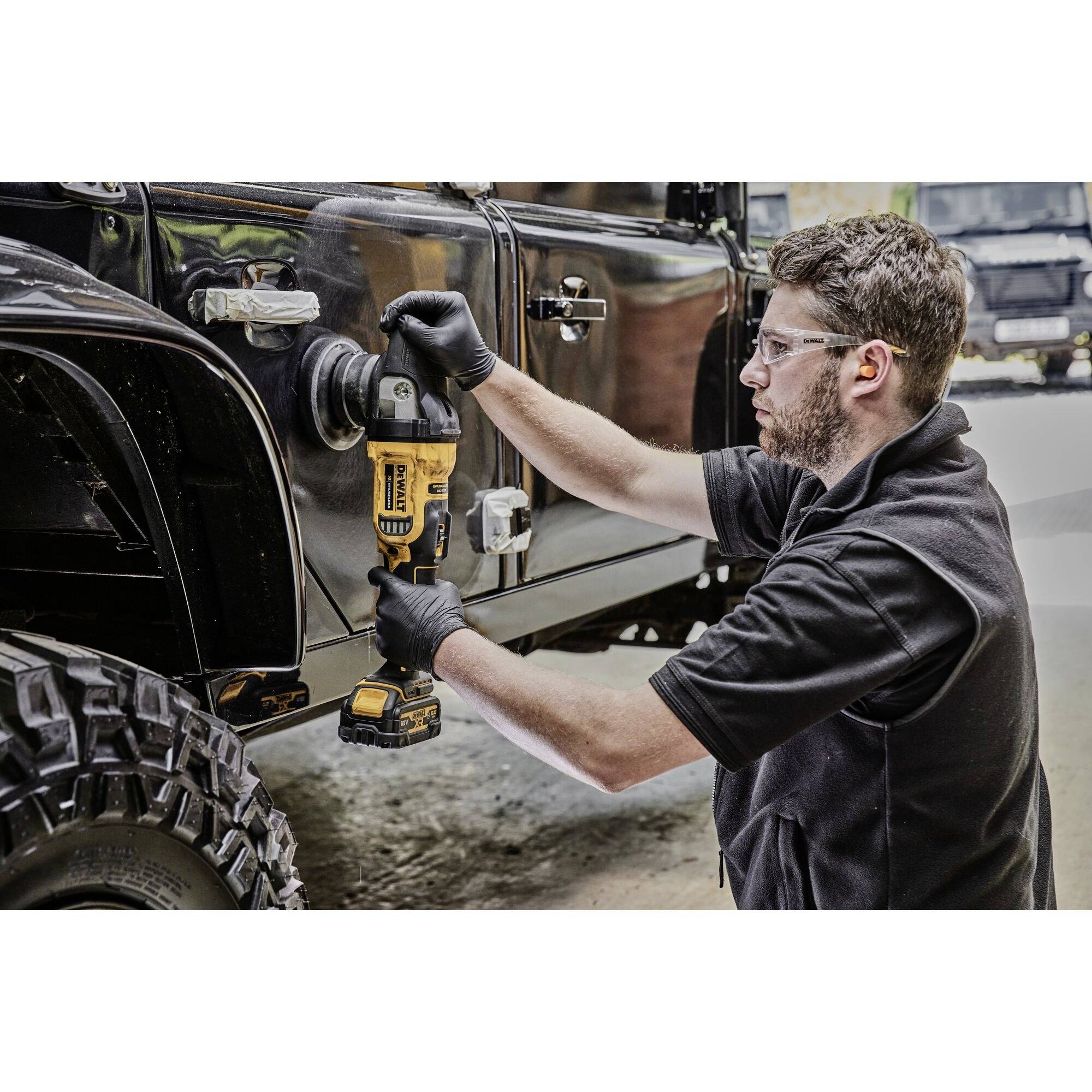 A man in black clothing is repairing the wing of a black off-road vehicle with a drill in a workshop.