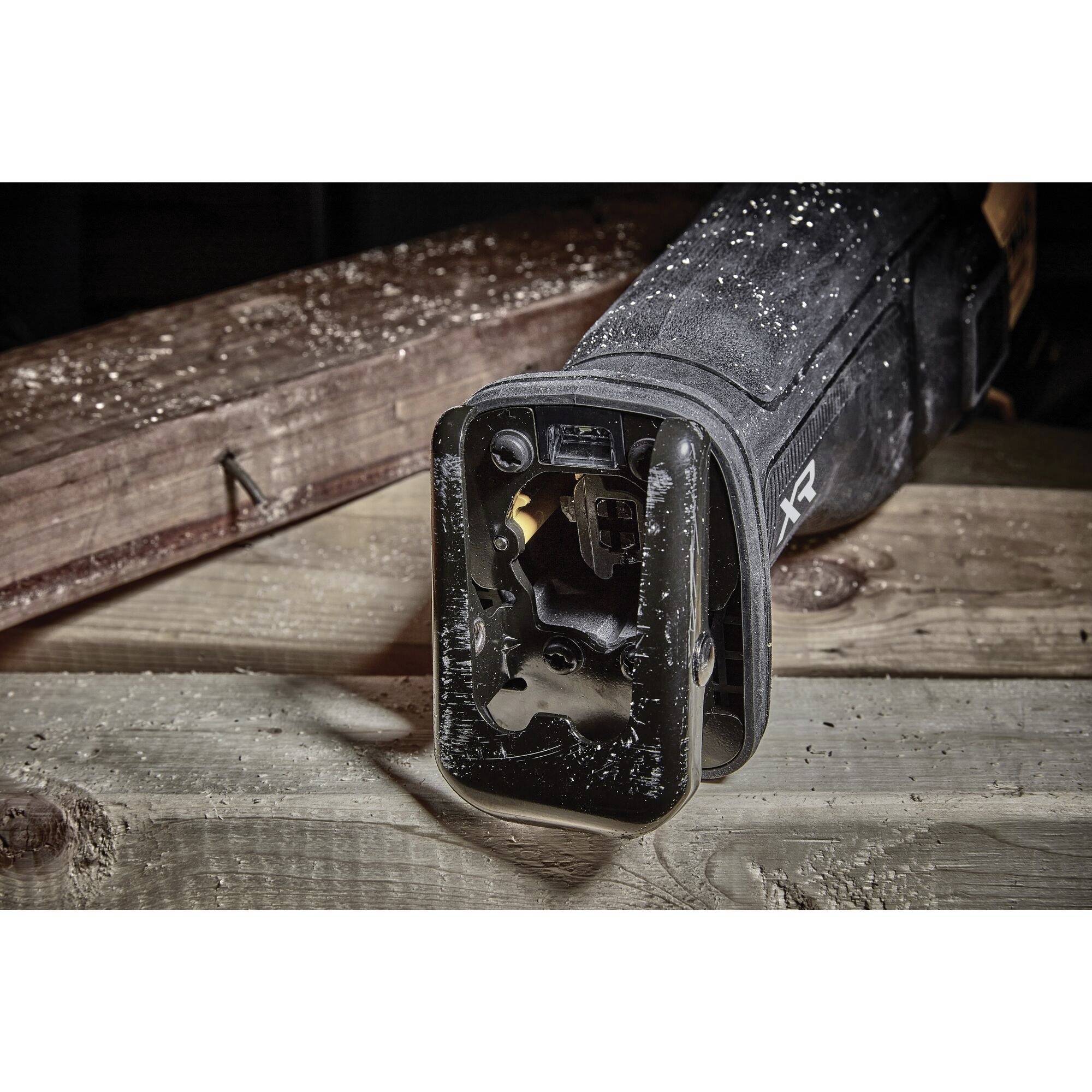 An electric saw lies on a wooden table, surrounded by sawdust. The saw is black, with its blade in the foreground.