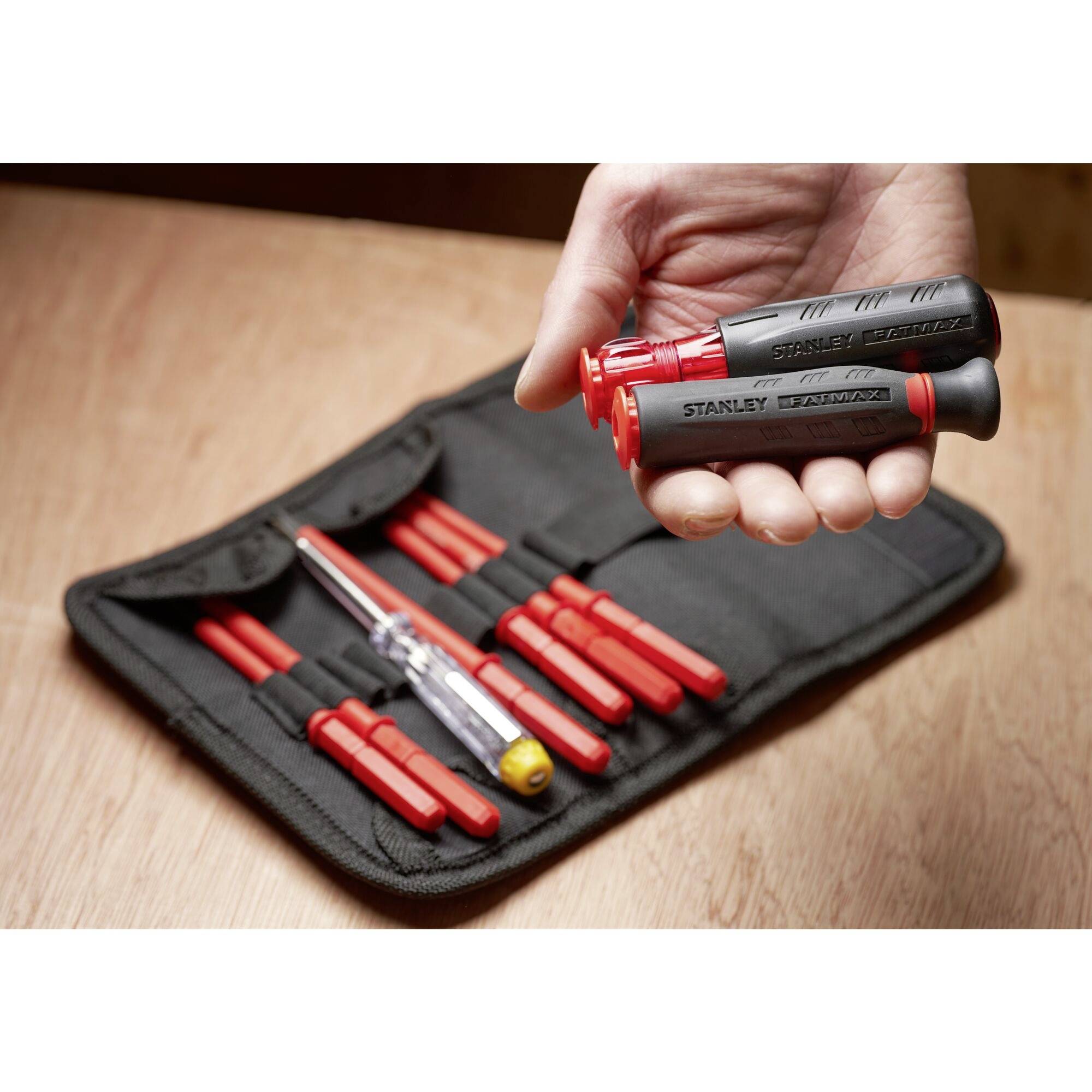 A hand is holding a black and red Stanley screwdriver. In the background, an opened tool bag contains several screwdrivers.