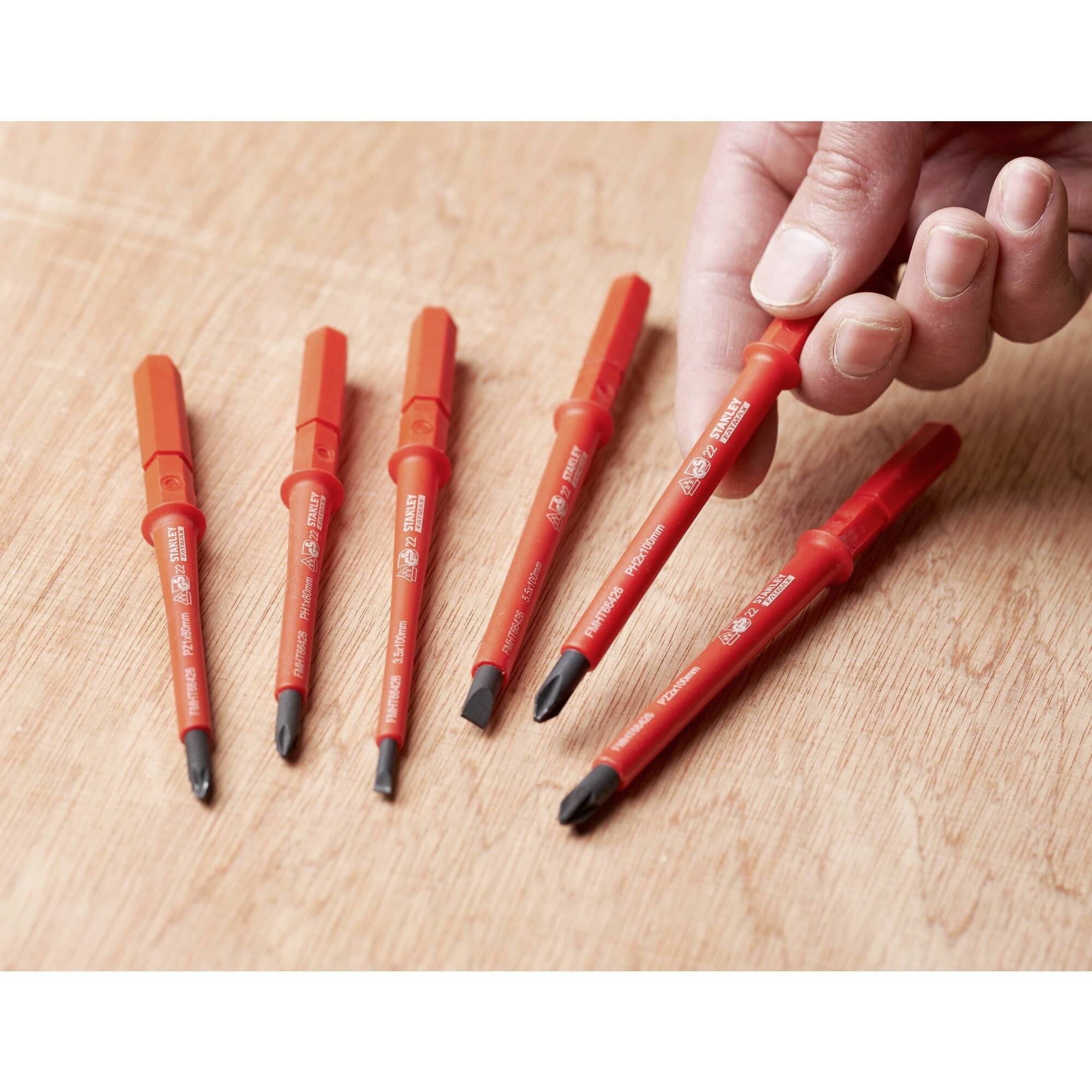 Six red screwdriver blades on a wooden surface; a hand is lifting one blade.
