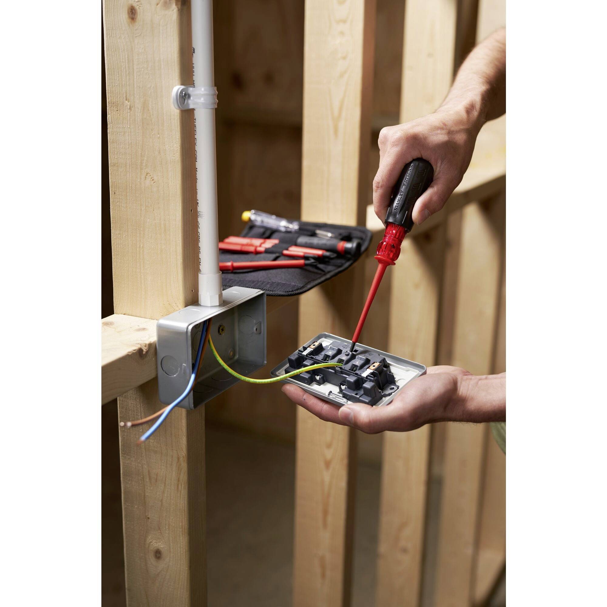 A person is installing a socket in a wooden frame using a screwdriver. Cables are connected to the back of the socket.