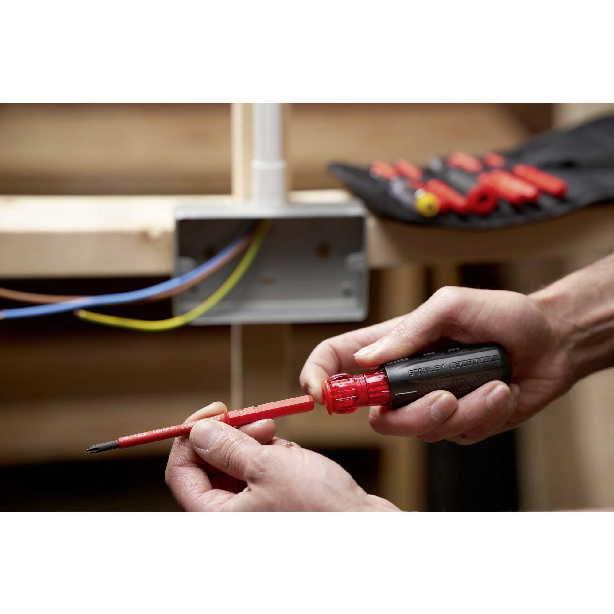 A person is repairing a cable in an electrical socket using a screwdriver. Additional tools are lying in the background.