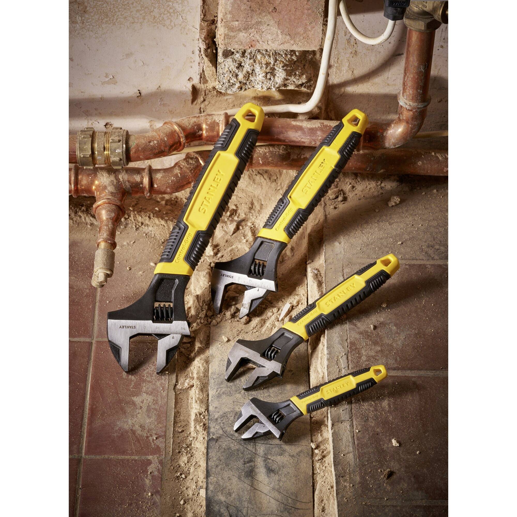 Four adjustable spanners with yellow handles lie on a dusty floor beside pipework.
