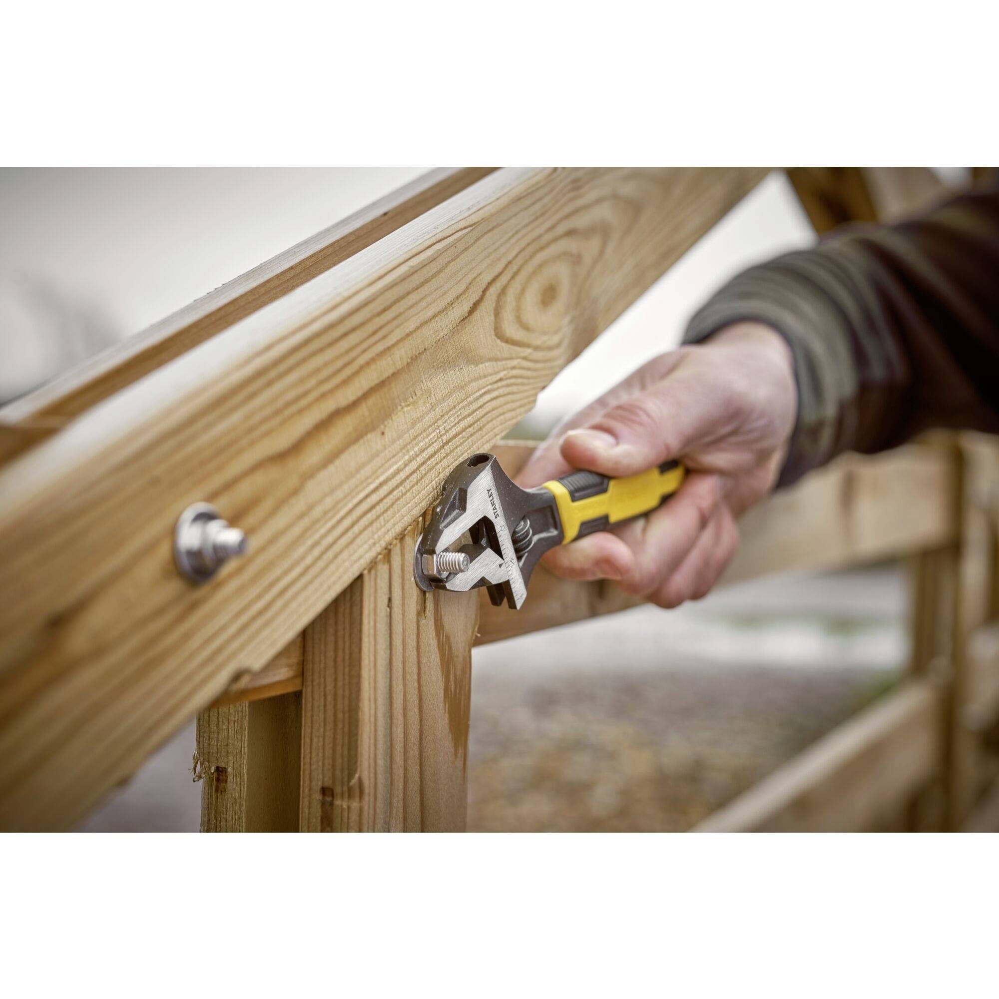 'A person is using an adjustable spanner to fasten a wooden plank of a fence. Focus is on the tool and hand.'