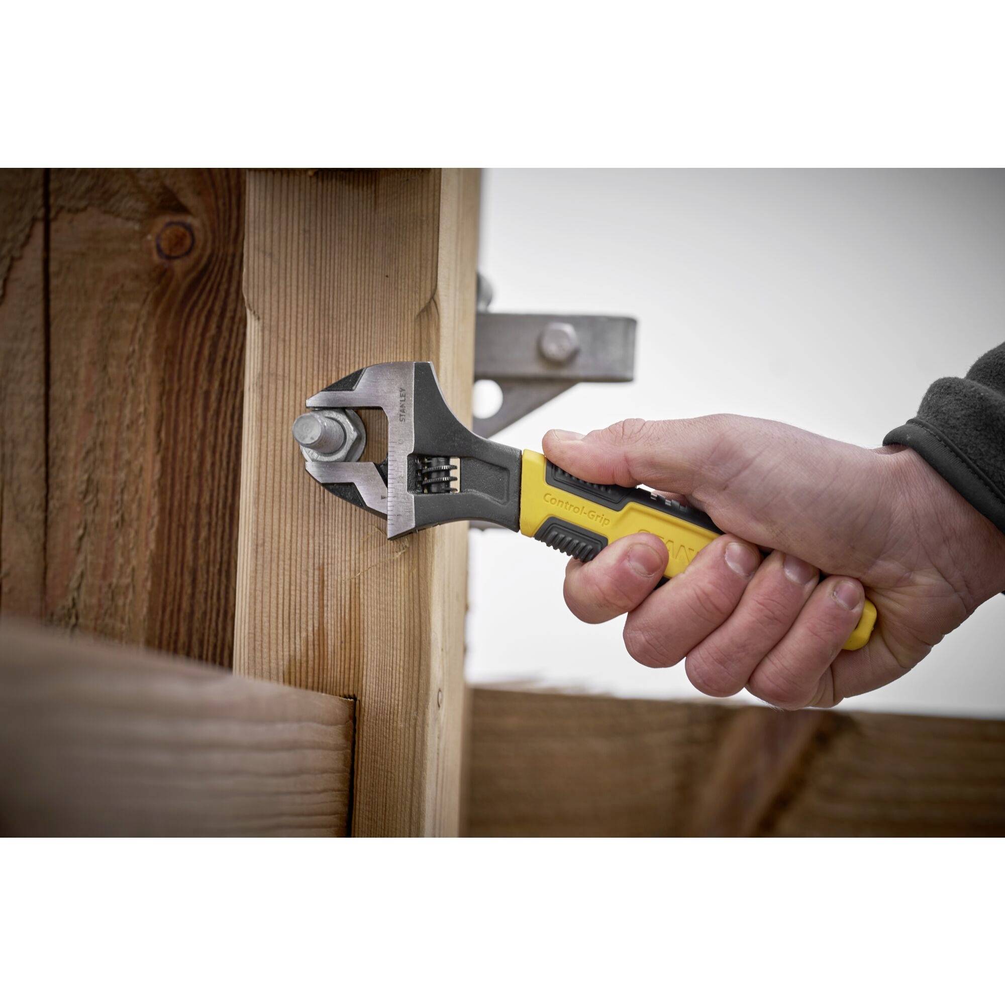 A hand holds a yellow adjustable spanner, tightening a metal nut on a wooden post.