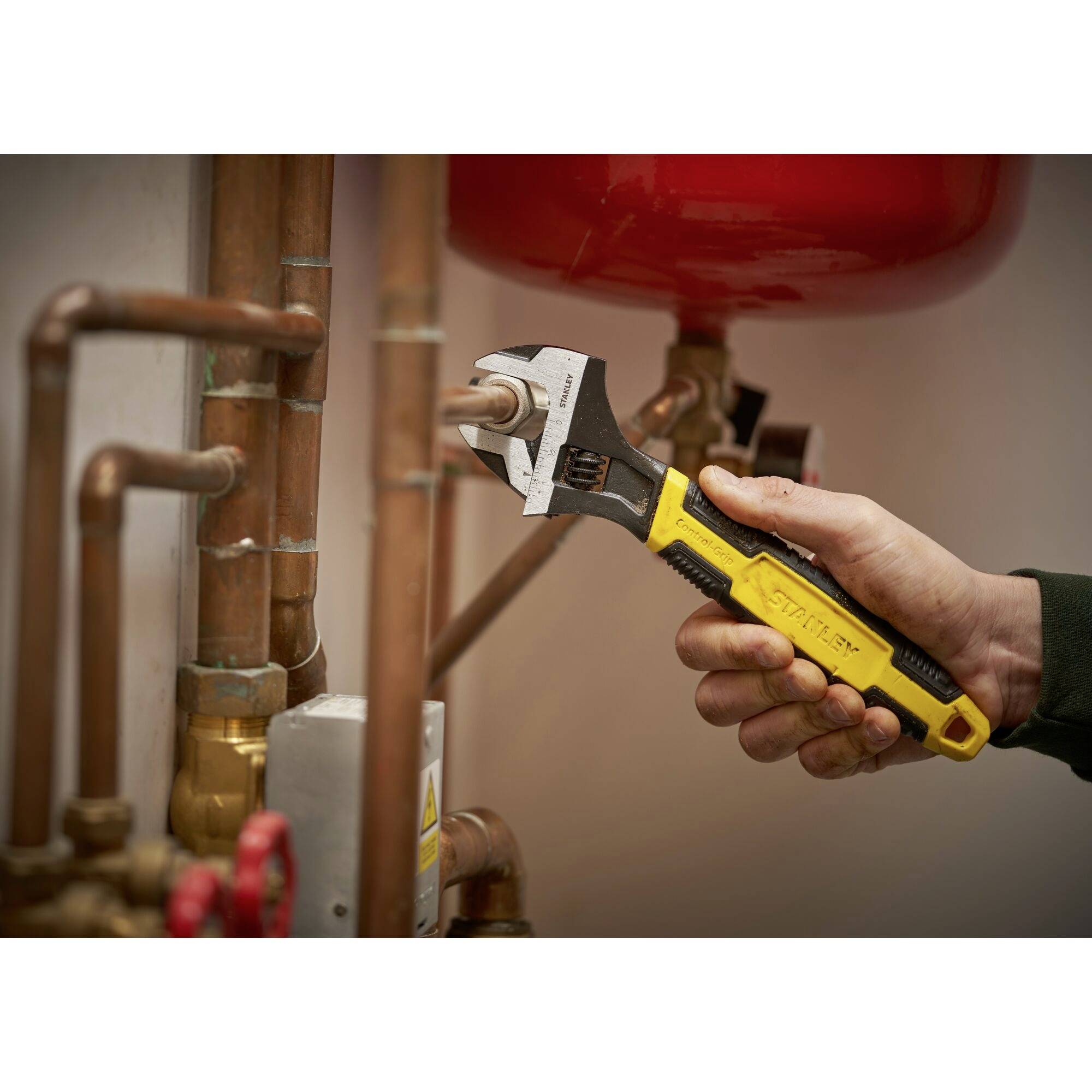 A hand adjusts a pipe valve with an adjustable spanner next to copper pipes.