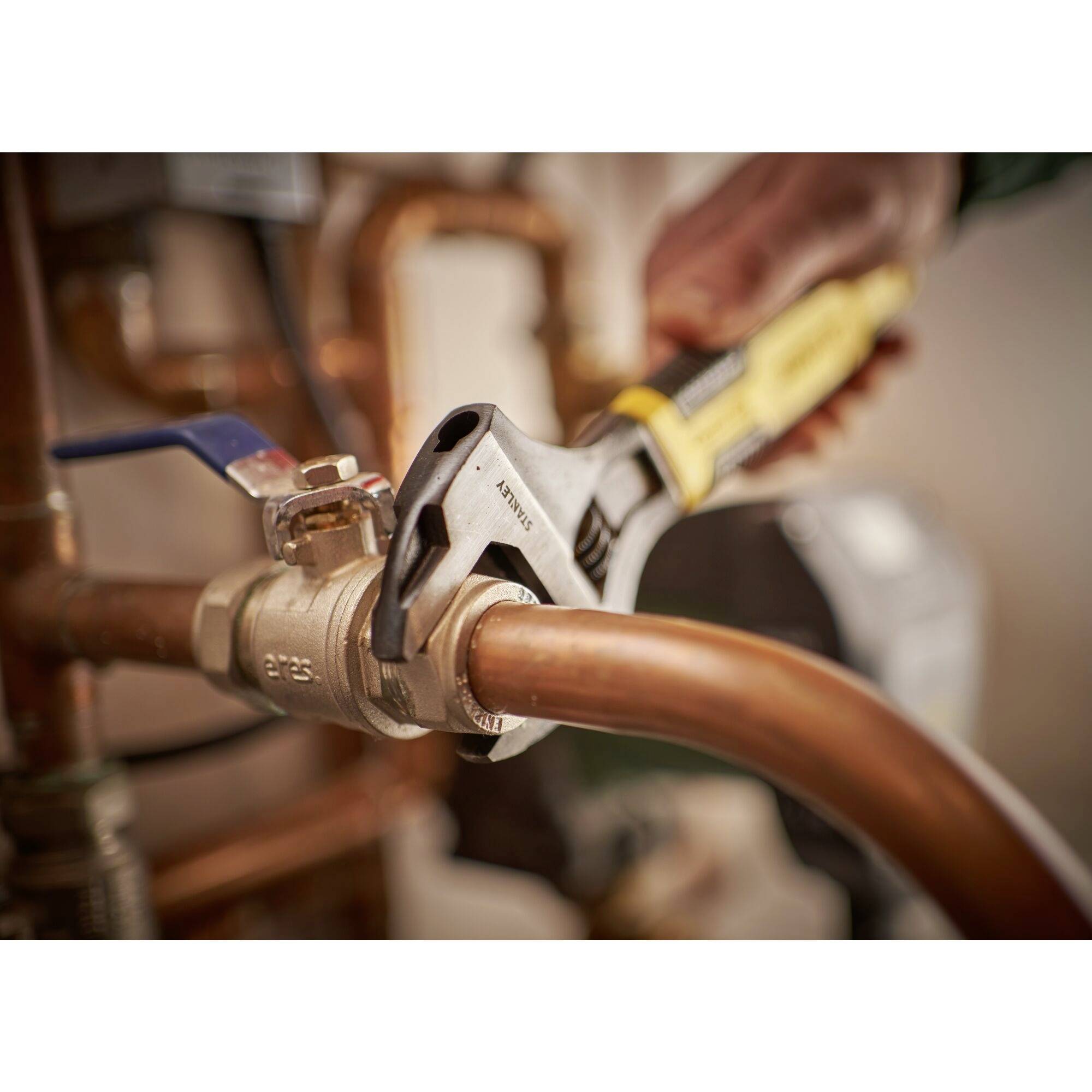 A hand holds a spanner and tightens a valve on a copper pipe. It is a plumbing installation.
