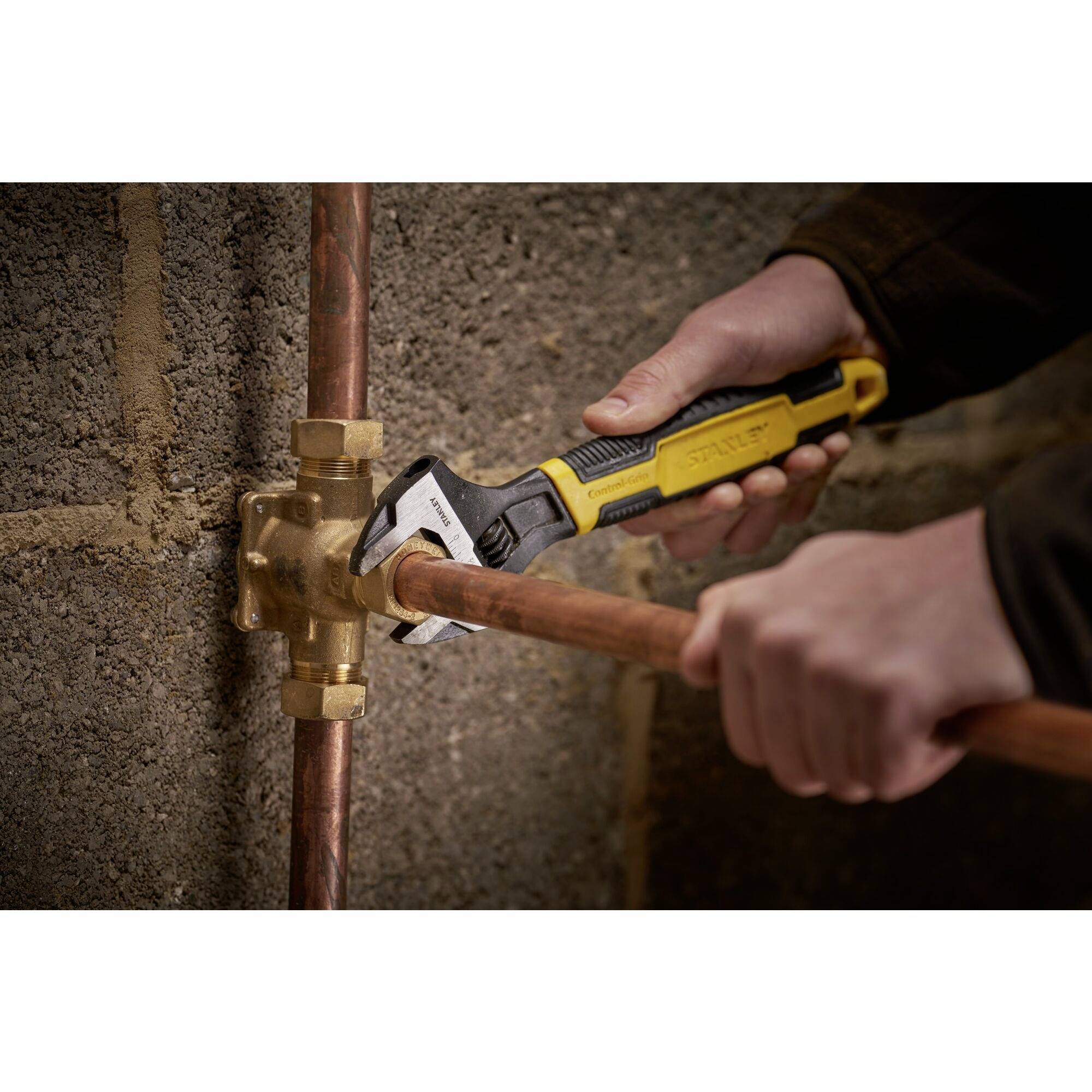 A person is using an adjustable spanner to secure a copper pipe to a valve in a wall-mounted installation.