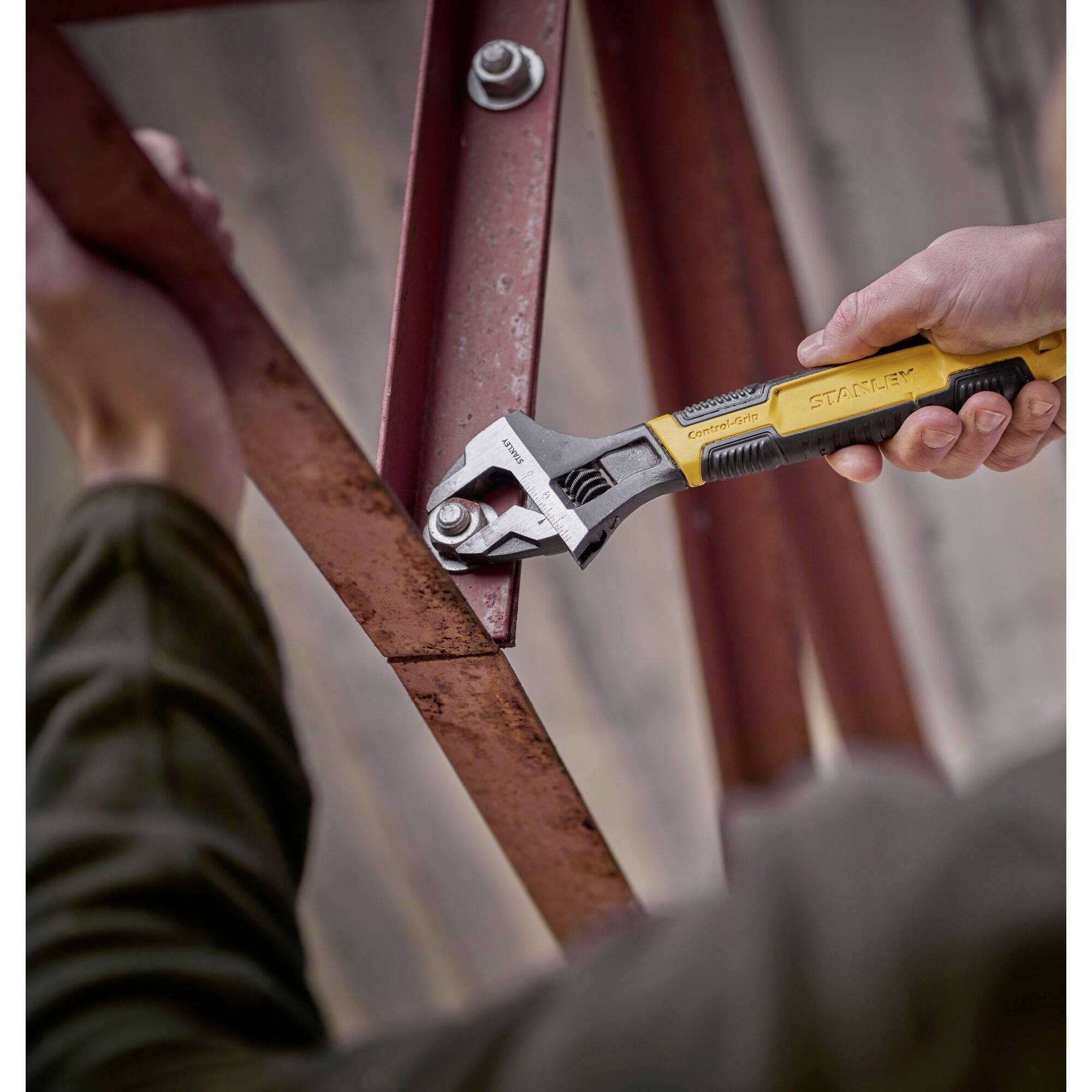 A person is tightening a screw on a rust-brown metal beam using an adjustable spanner.