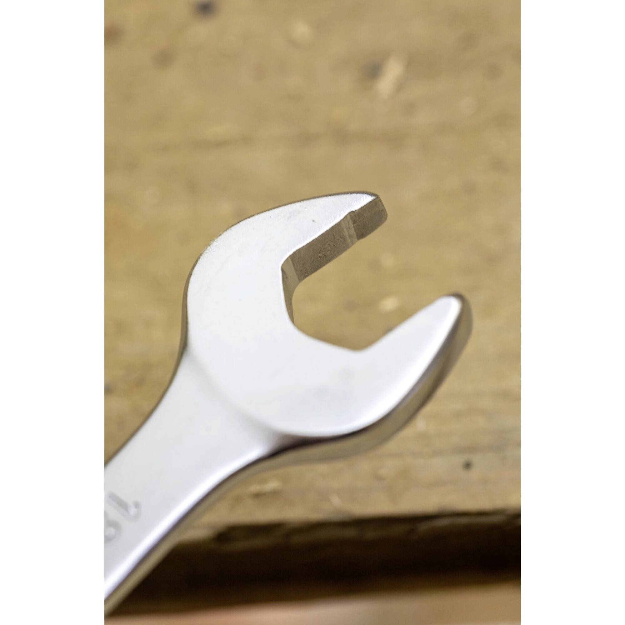 A silver spanner lies on a wooden surface.<br><br>Note: In British English, "wrench" is more commonly used for some contexts, but "spanner" is the standard British term for this type of tool.