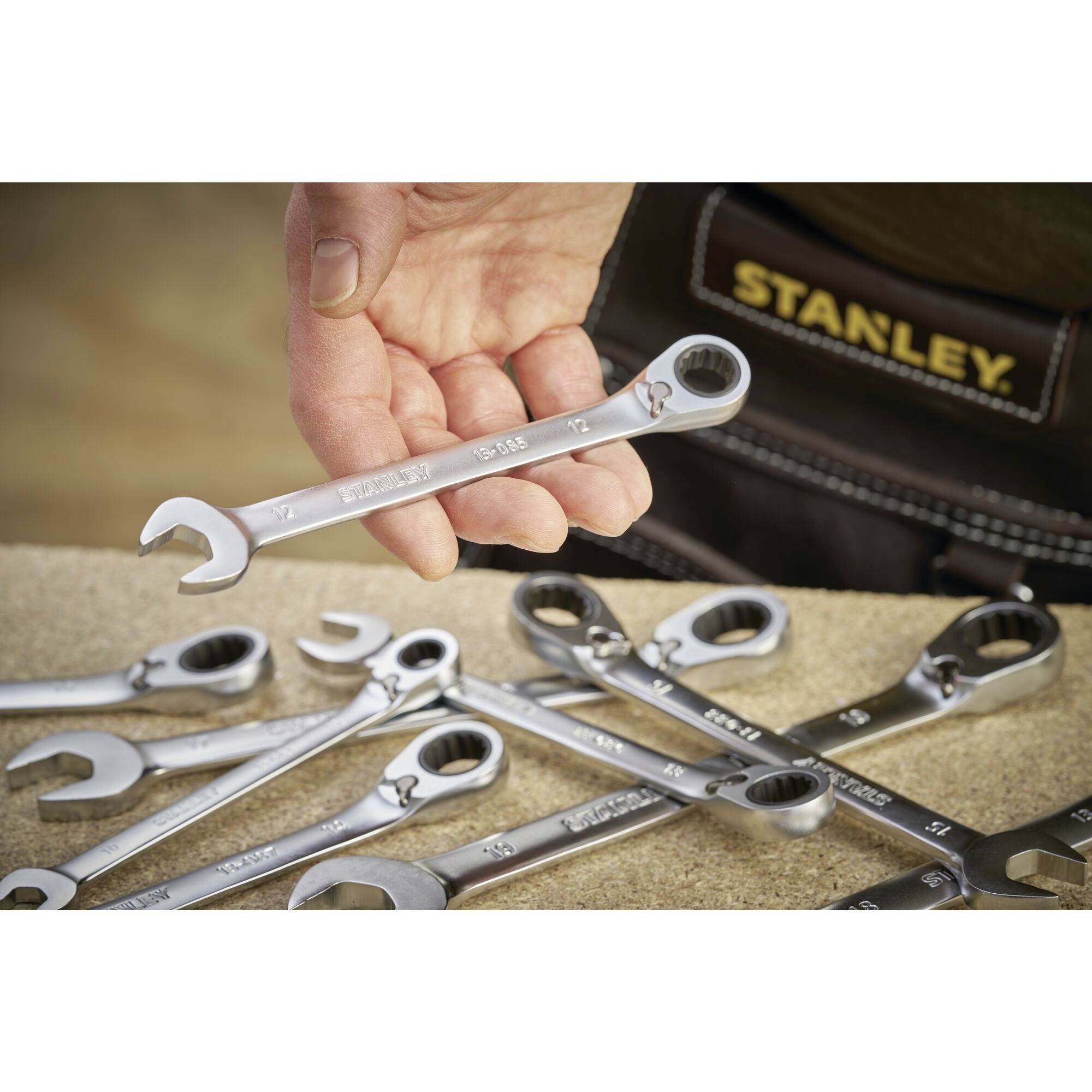 A hand is holding a spanner with '11' written on it over a table full of other spanners. A Stanley belt is visible in the background.