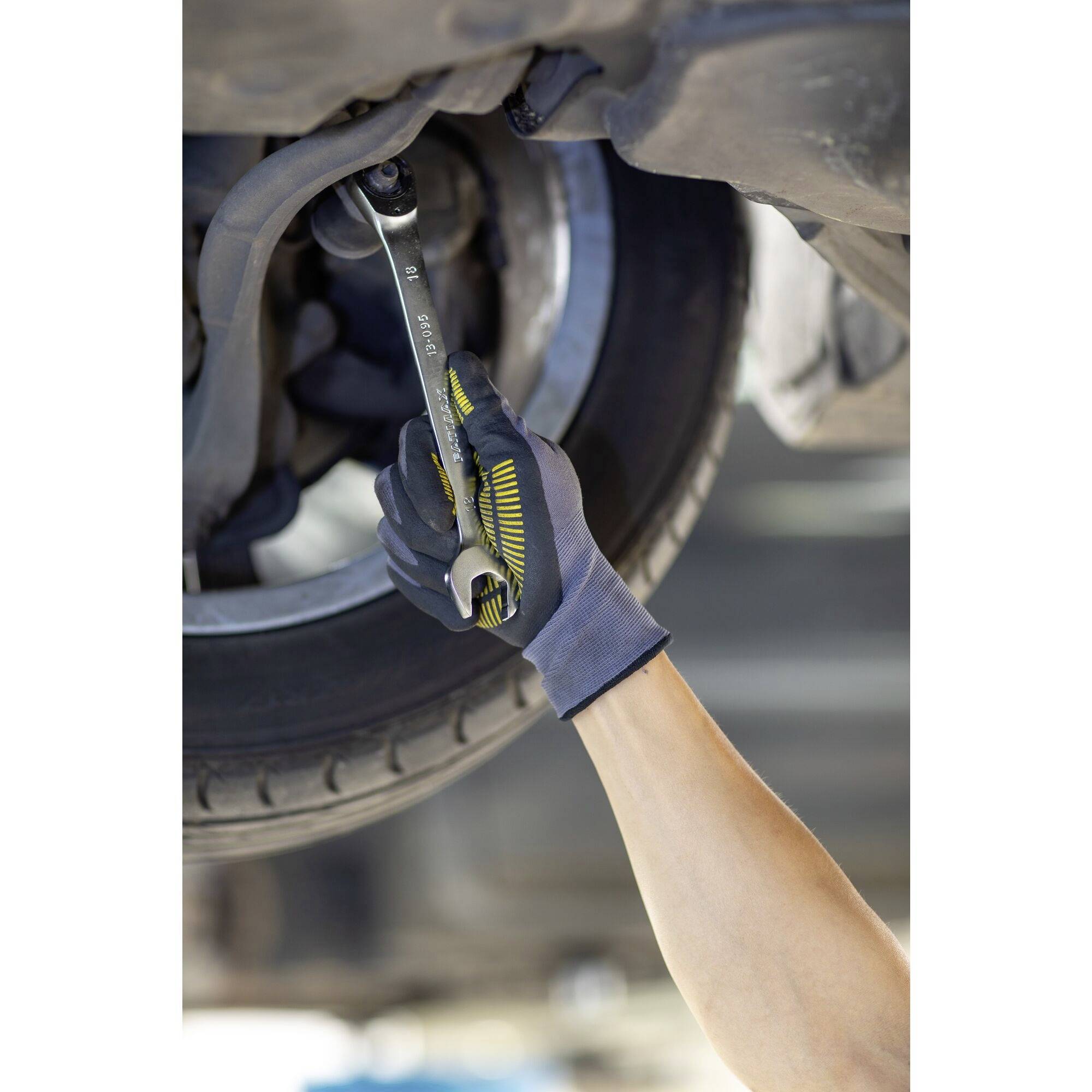 A hand wearing a glove holds a spanner and tightens a screw on a car tyre. The focus is on repair work.