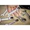 A hand is holding a small ring key, surrounded by several other keys on a workbench.
