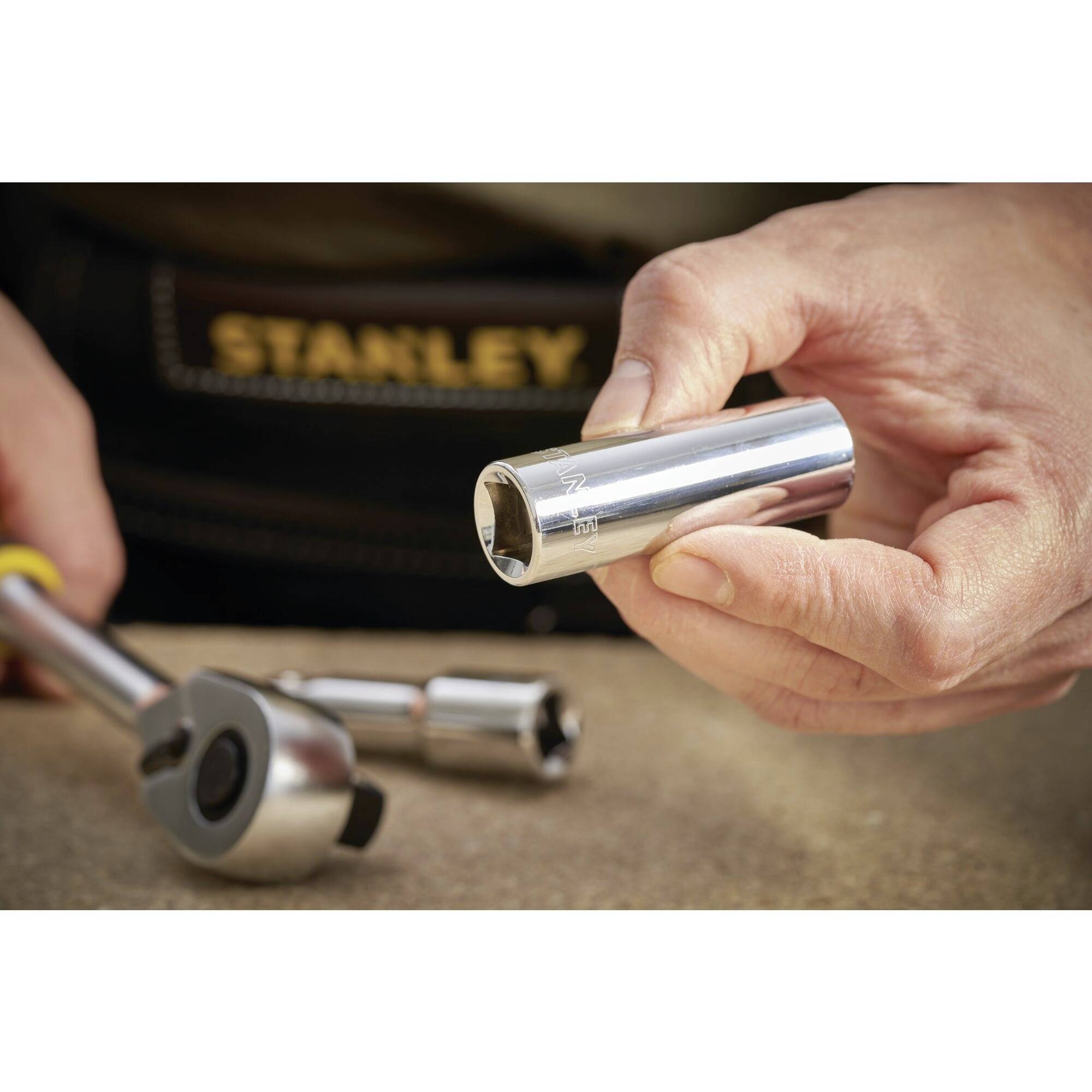 A hand is holding a metal hex key, with a spanner lying in the background. The 'STANLEY' logo is visible in the background.