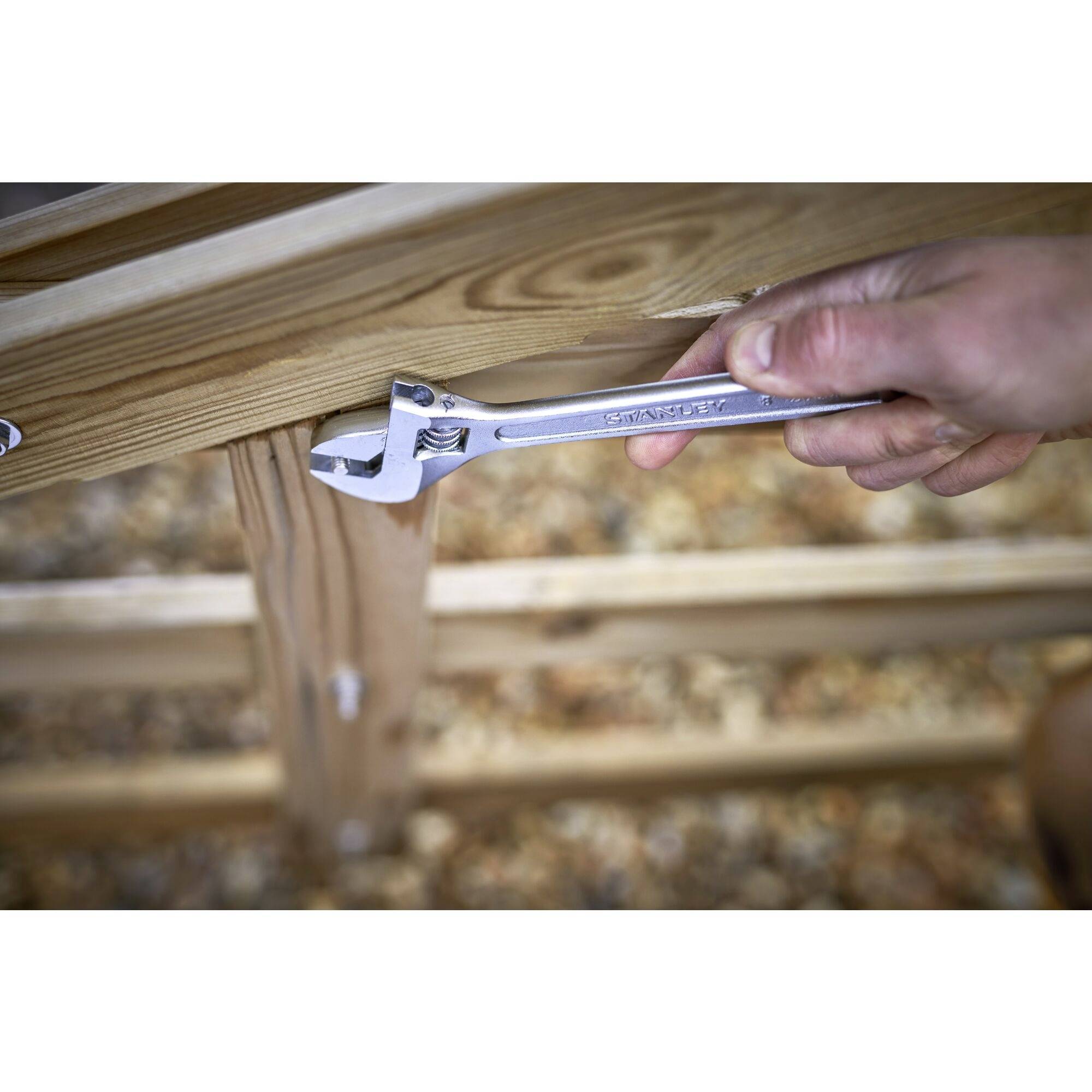 A person is tightening a screw on a wooden structure using an adjustable spanner.