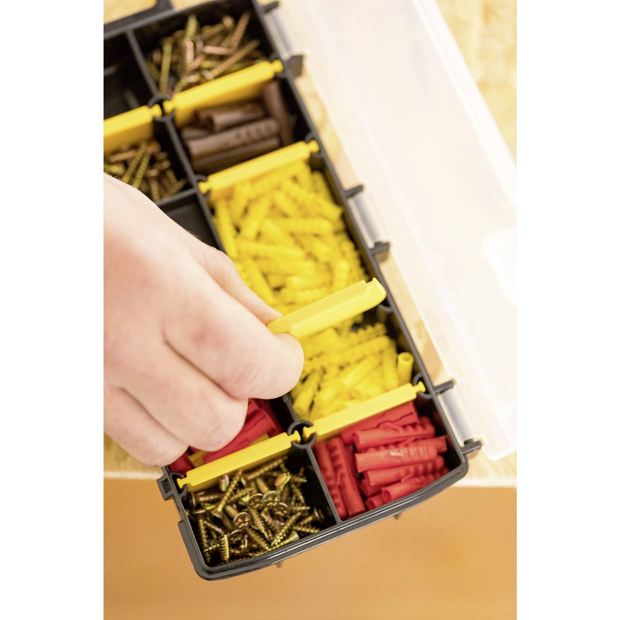 A hand reaches for a yellow plastic plug box in an organiser, where red plugs and screws are also visible.