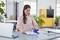 Woman at a desk, using a stapler to organise documents. In the background, office plants and shelves are visible.