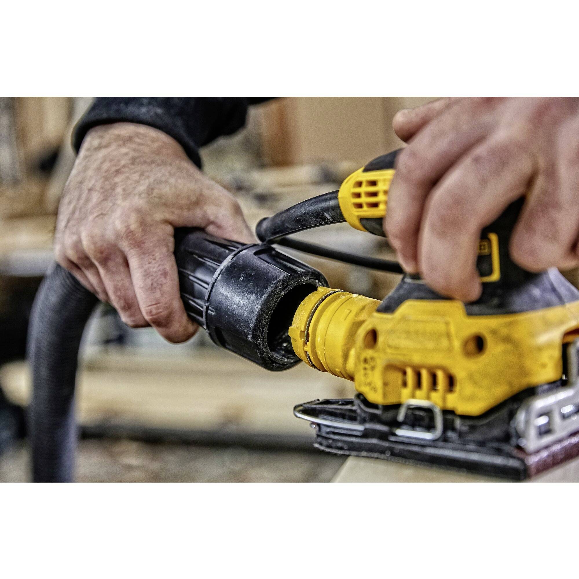 A person is holding an electric orbital sander. Hands are securing the tool while it works on a wooden table.