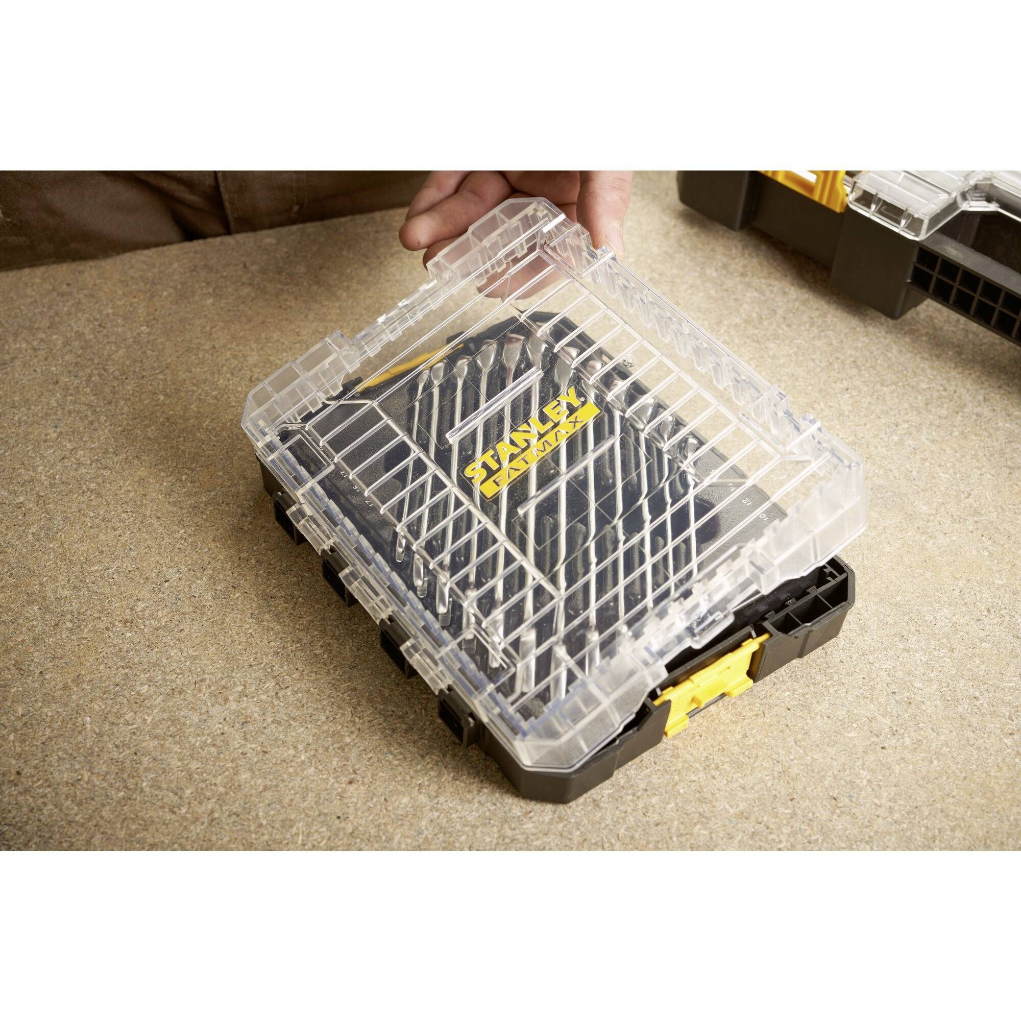 A clear plastic box contains a tool set with a brand logo on the front. A hand reaches for the box.