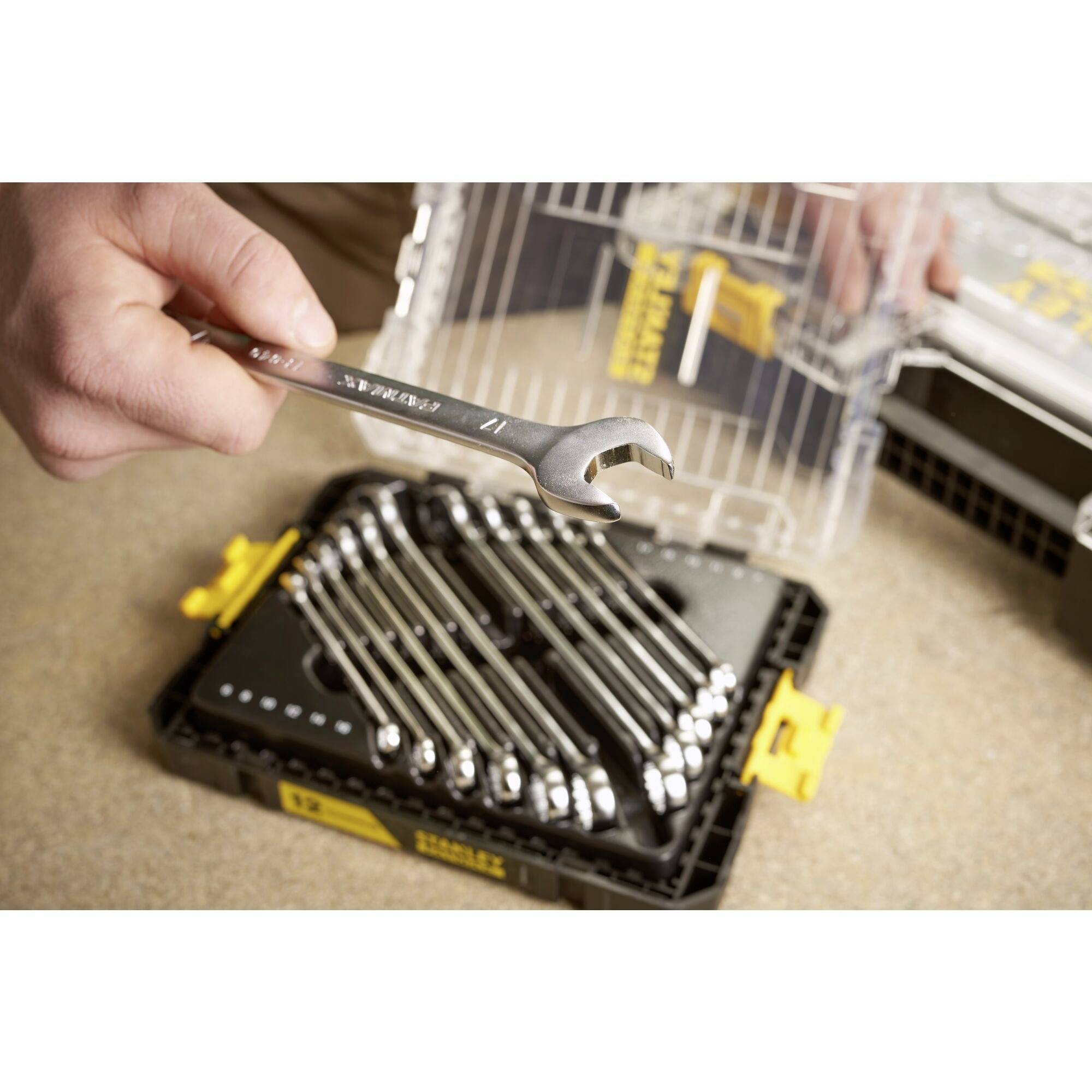 A hand holds a spanner over an open toolbox with several spanners.