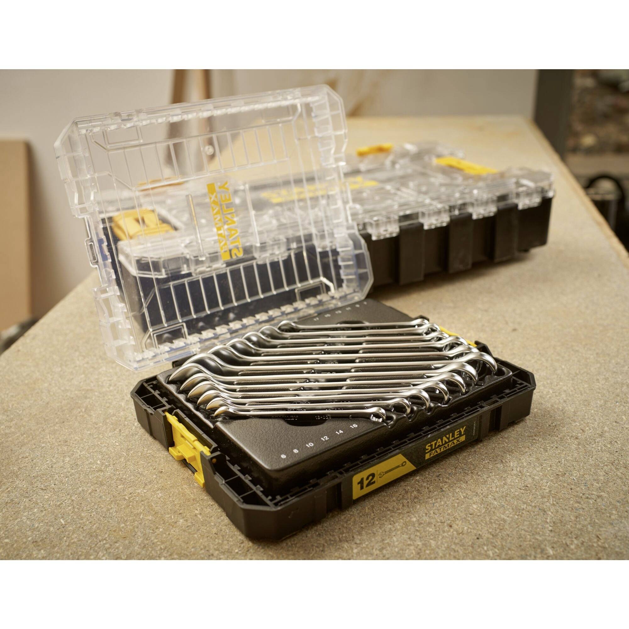 Set of 12 open ring spanners in a transparent black box on a workbench. Background shows open box.