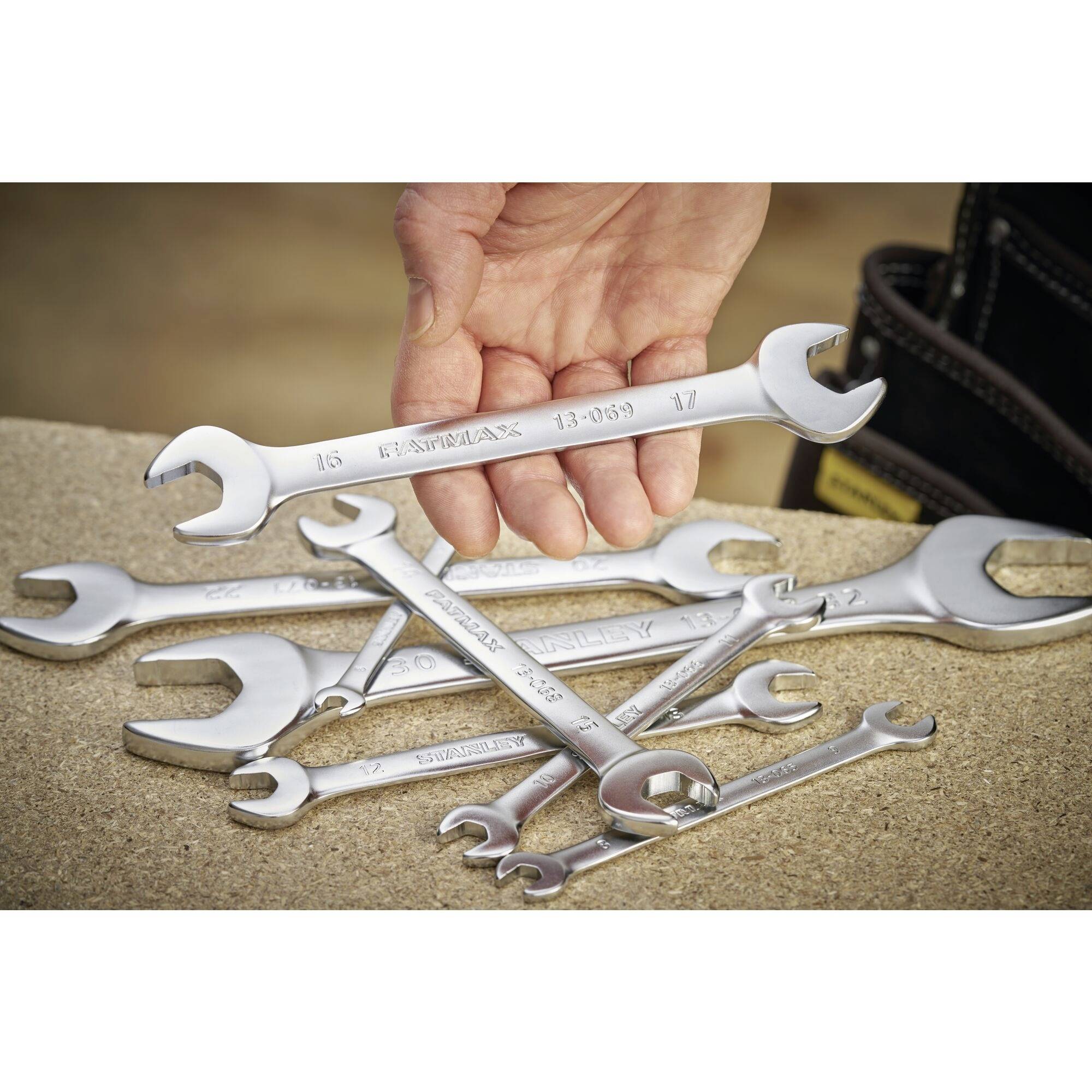 A stack of open spanners on a workbench, with a hand holding a 17-mm spanner. Tools are scattered in the background.