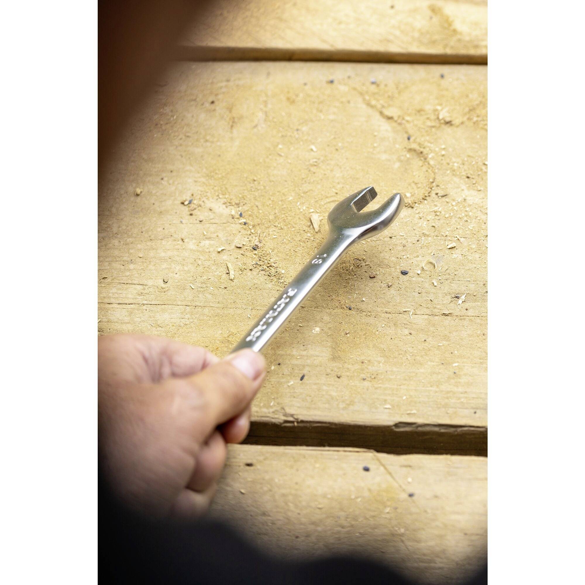 A spanner is being held by a hand on a wooden table.