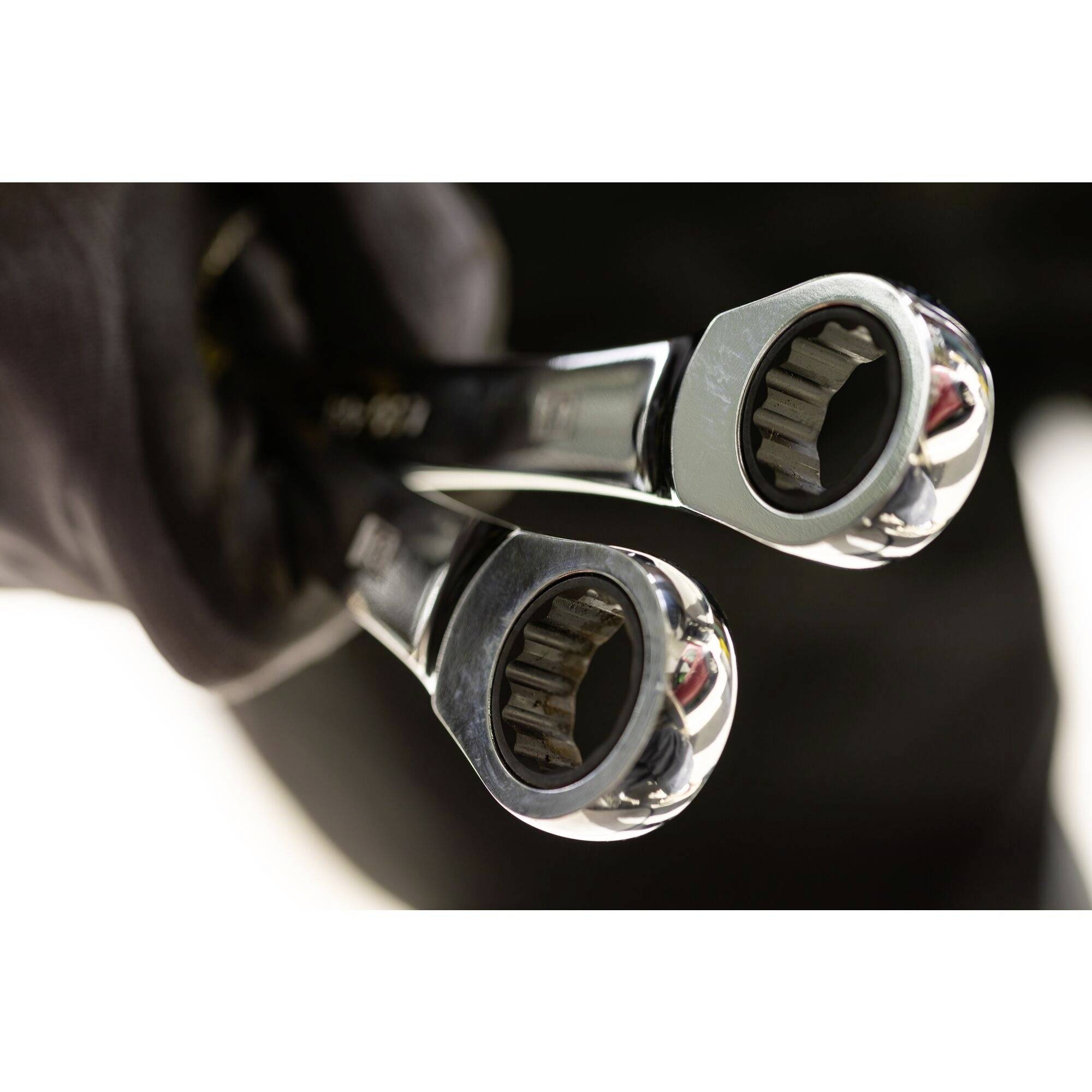 A hand holds two gleaming ring keys, ready for mechanical work, with focus on the tool heads.