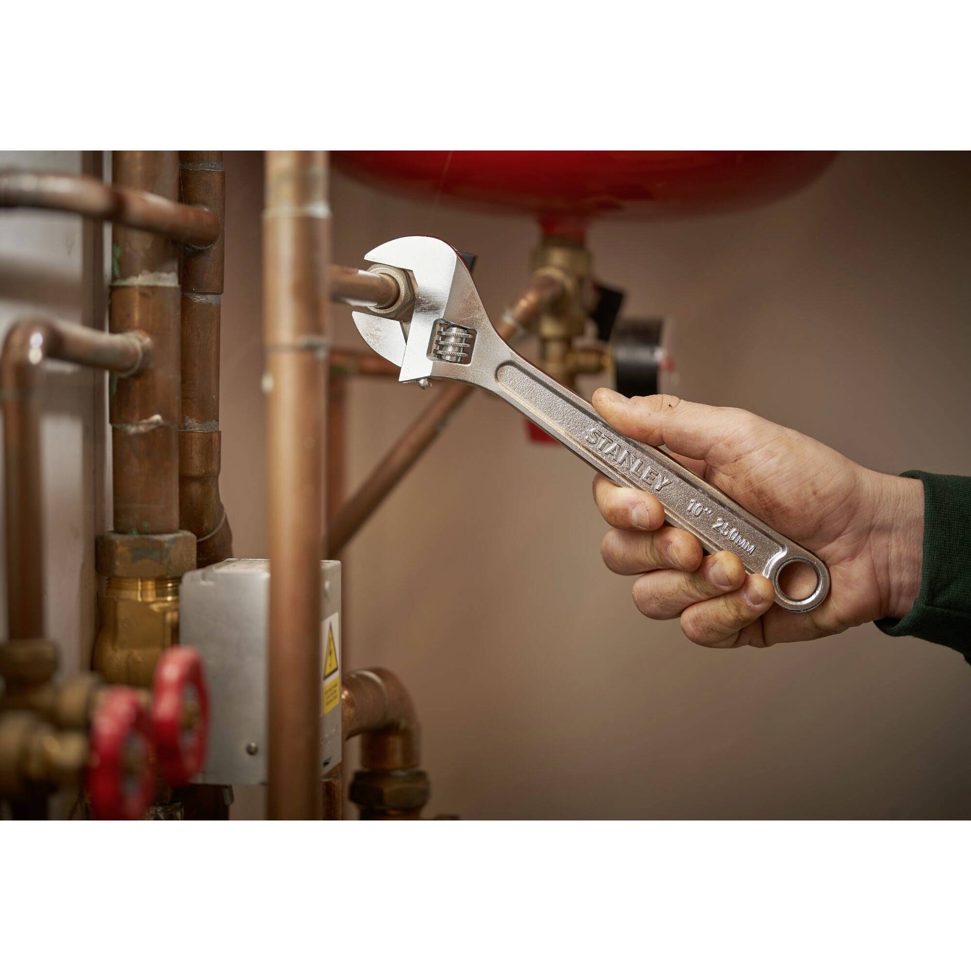 A person is tightening a pipe connection in a piping installation using an adjustable spanner.