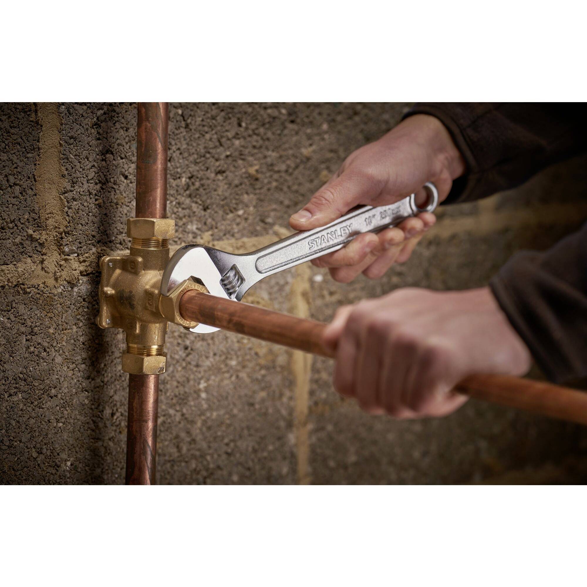 A person is repairing a copper pipe with a spanner at a brass-coloured valve. Hands are focused.