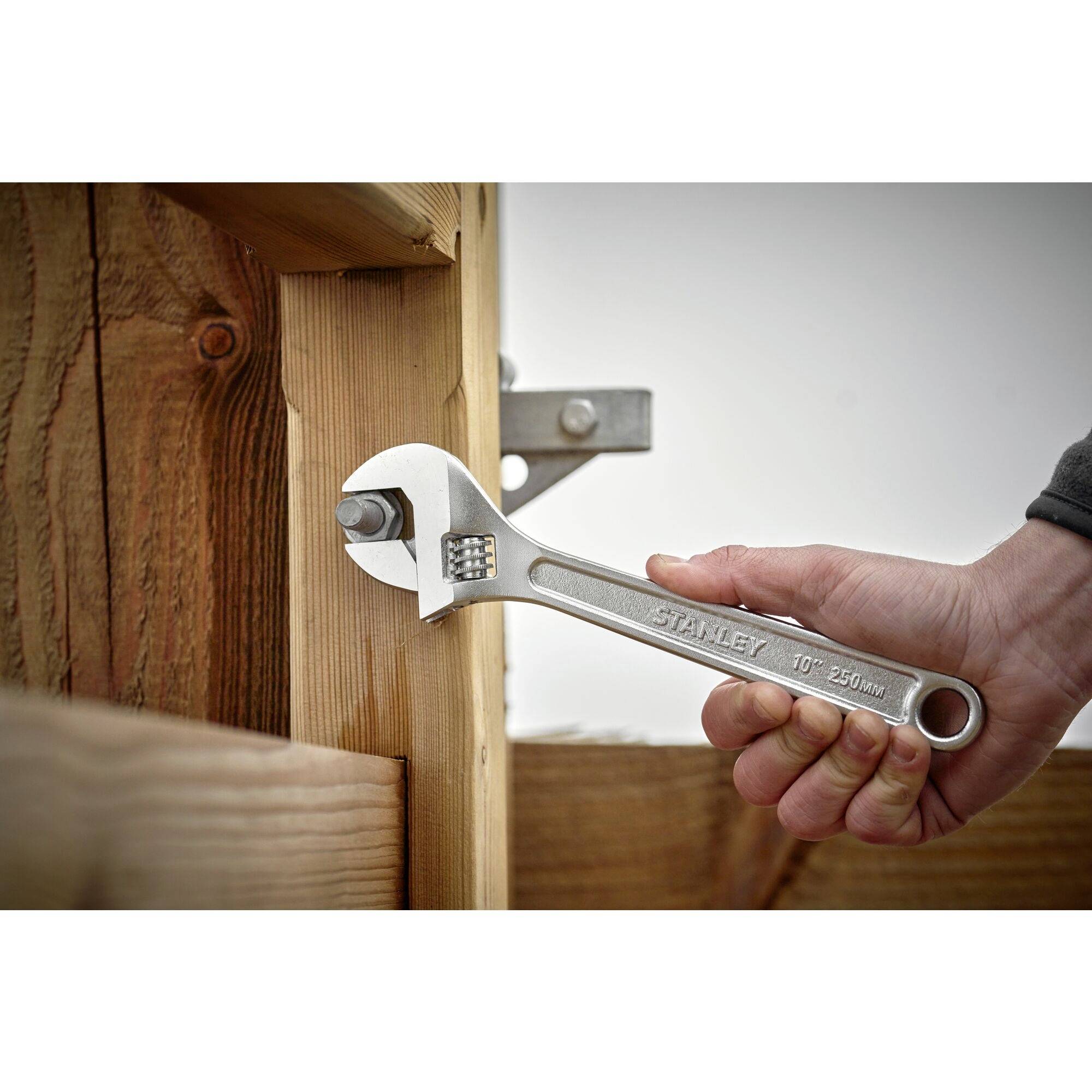 A person is tightening a nut on a wooden joint using an adjustable spanner.