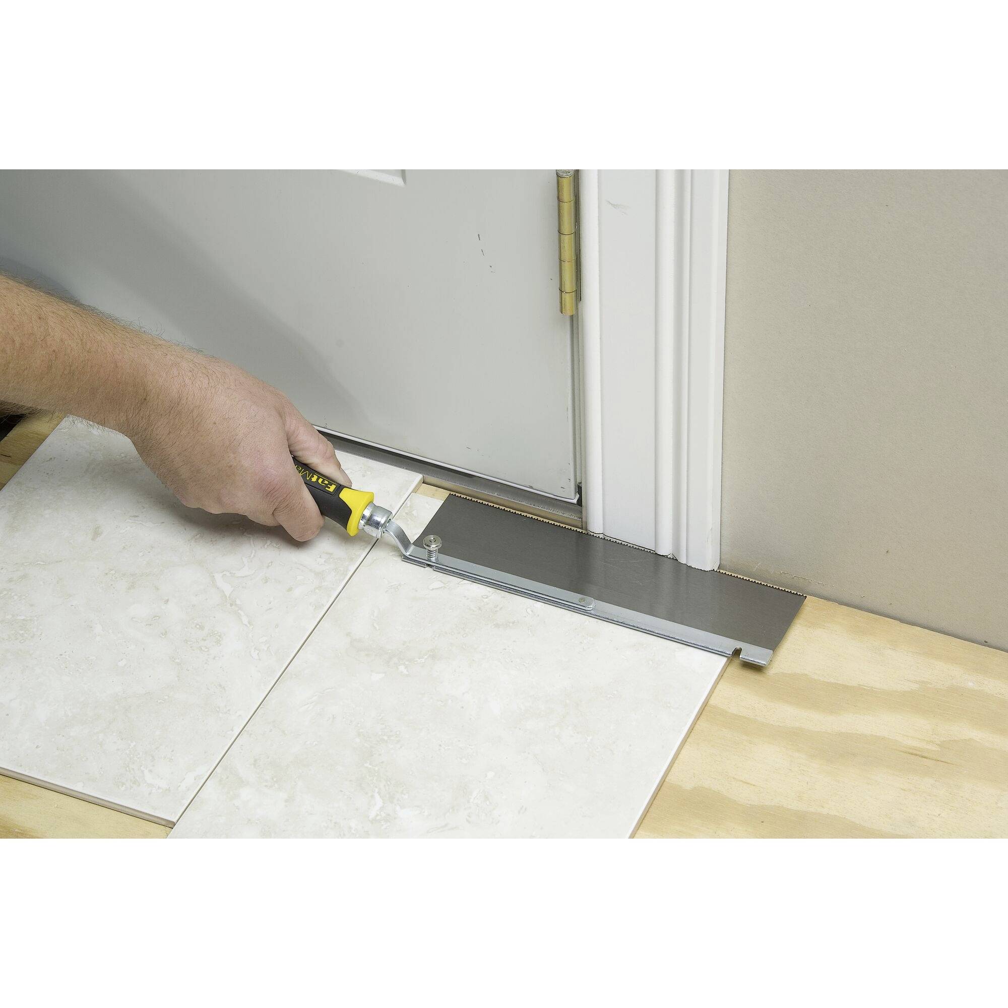 A tradesman is adjusting tiles to a door threshold with a saw and levelling the height to ensure correct tile installation.