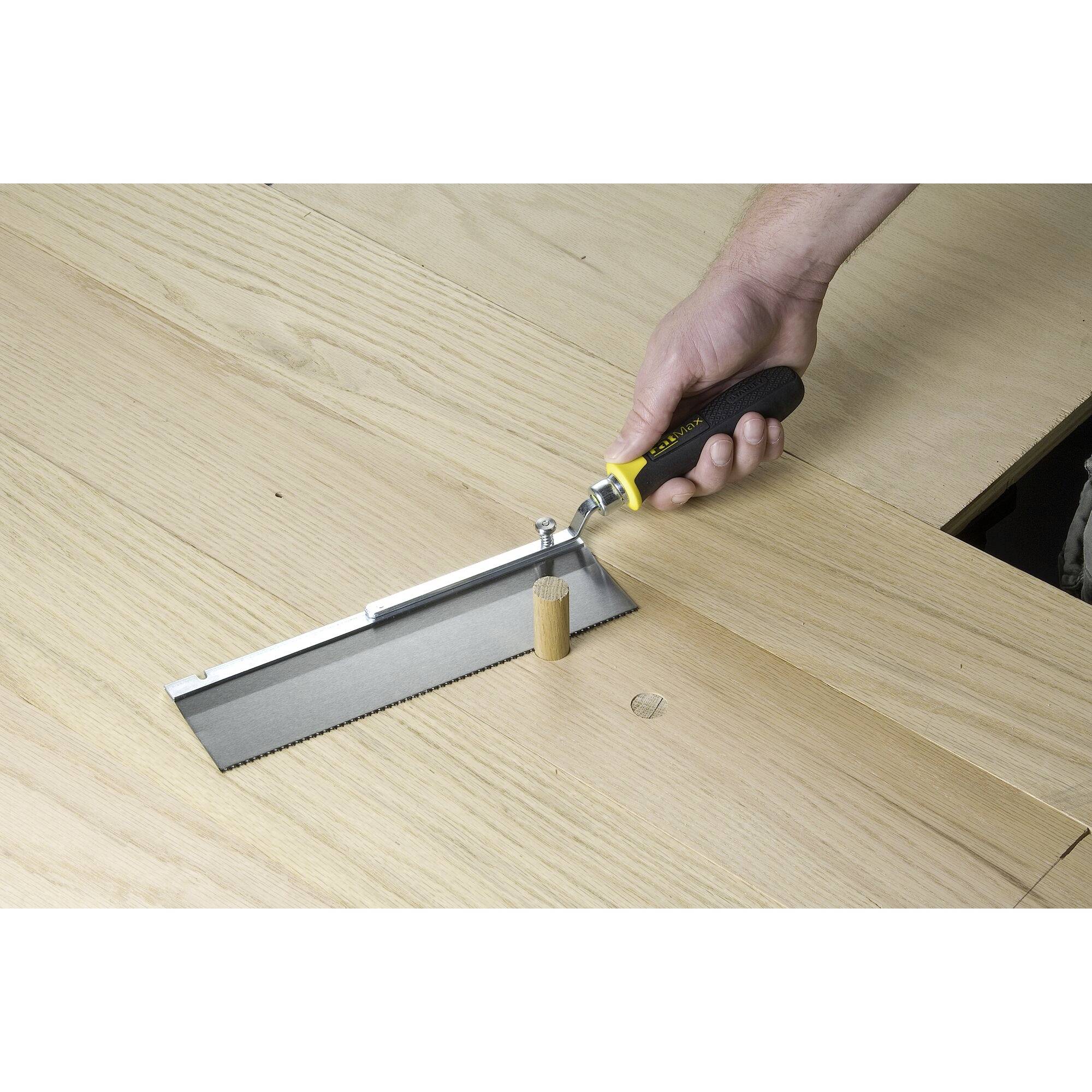 A hand holds a folding saw and cuts a dowel flush with the wooden surface.