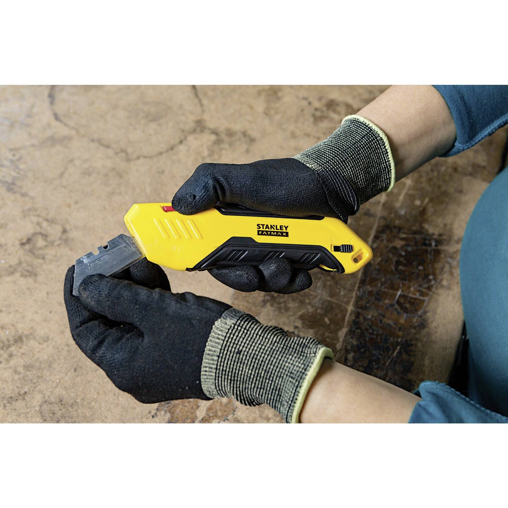 A person wearing gloves is holding a yellow Stanley utility knife and cutting something on a table.