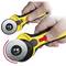 A hand is holding a yellow rotary cutter. A red arrow indicates the direction for adjustment of the safety switch.