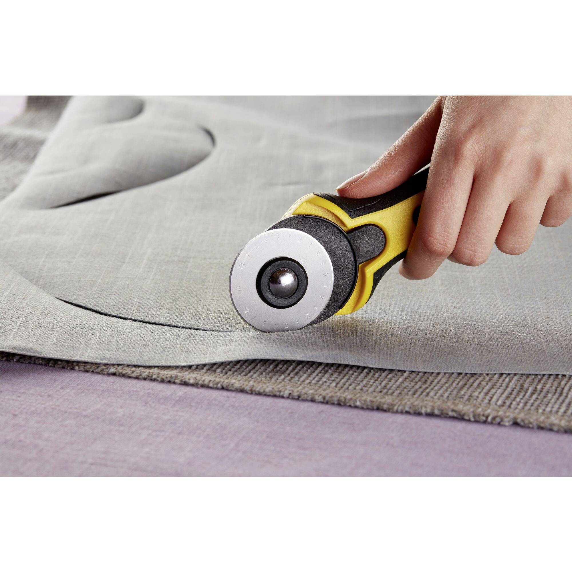 A hand is using a yellow rotary cutter to precisely follow a pattern on grey fabric.