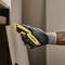 A hand wearing a work glove is holding a yellow Stanley knife and cutting a white board.