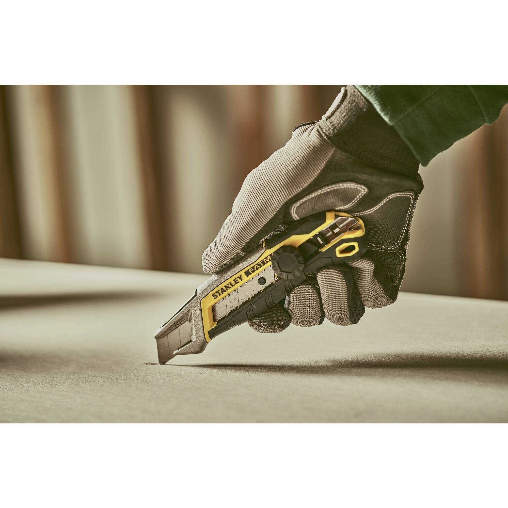 A gloved person is holding a yellow and black Stanley knife and cutting cardboard.