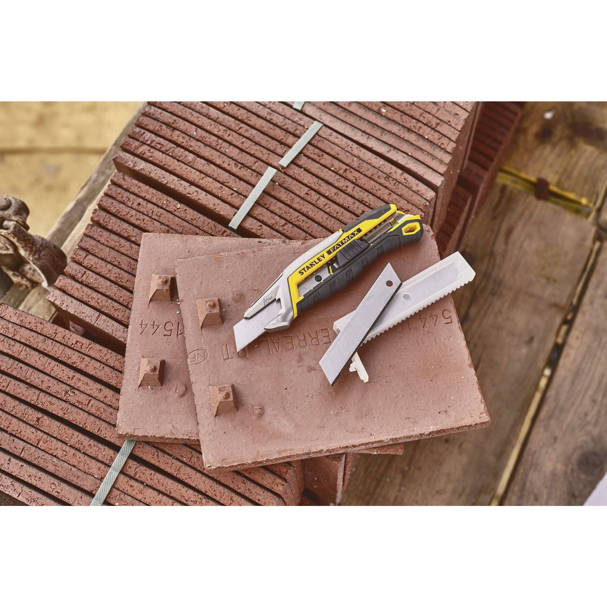 Bricks on a wooden pallet with two tools: a Stanley knife and a cardboard saw. Construction site in the background.