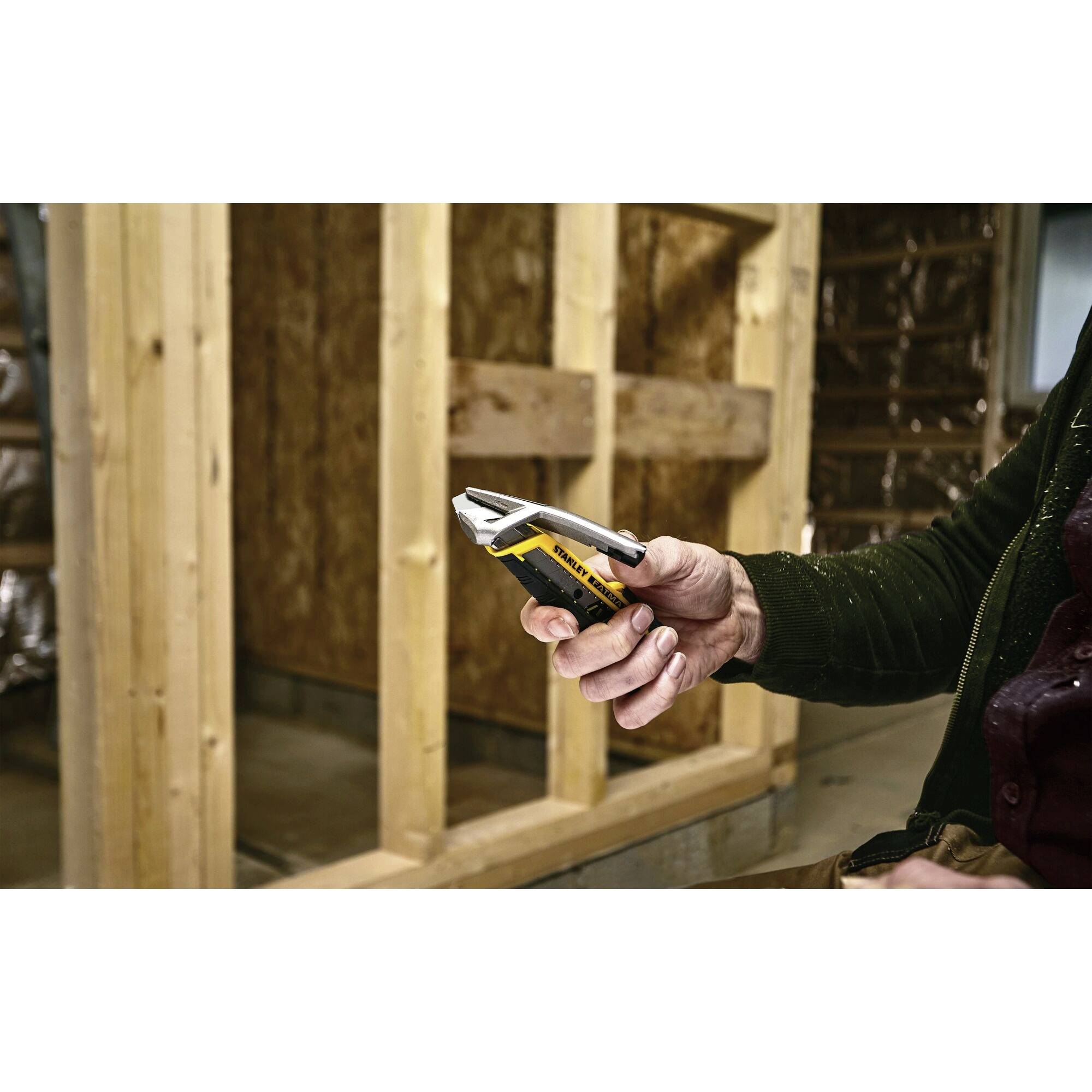 A person is holding a yellow and black pair of pliers at the top of a construction site in front of a wooden frame. Insulated walls are visible in the background.