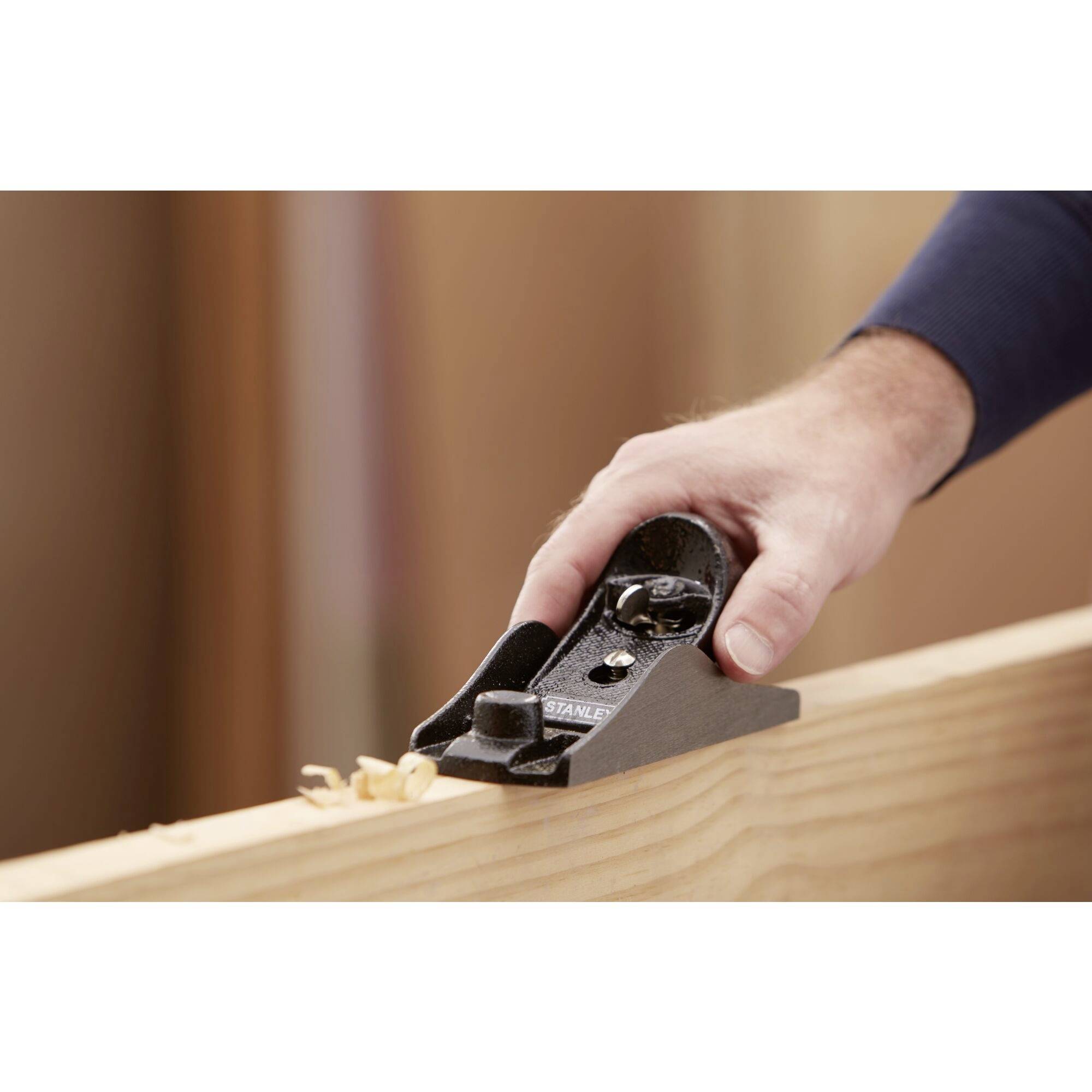 A hand holds a plane and smooths the surface of a wooden board, creating wood shavings.