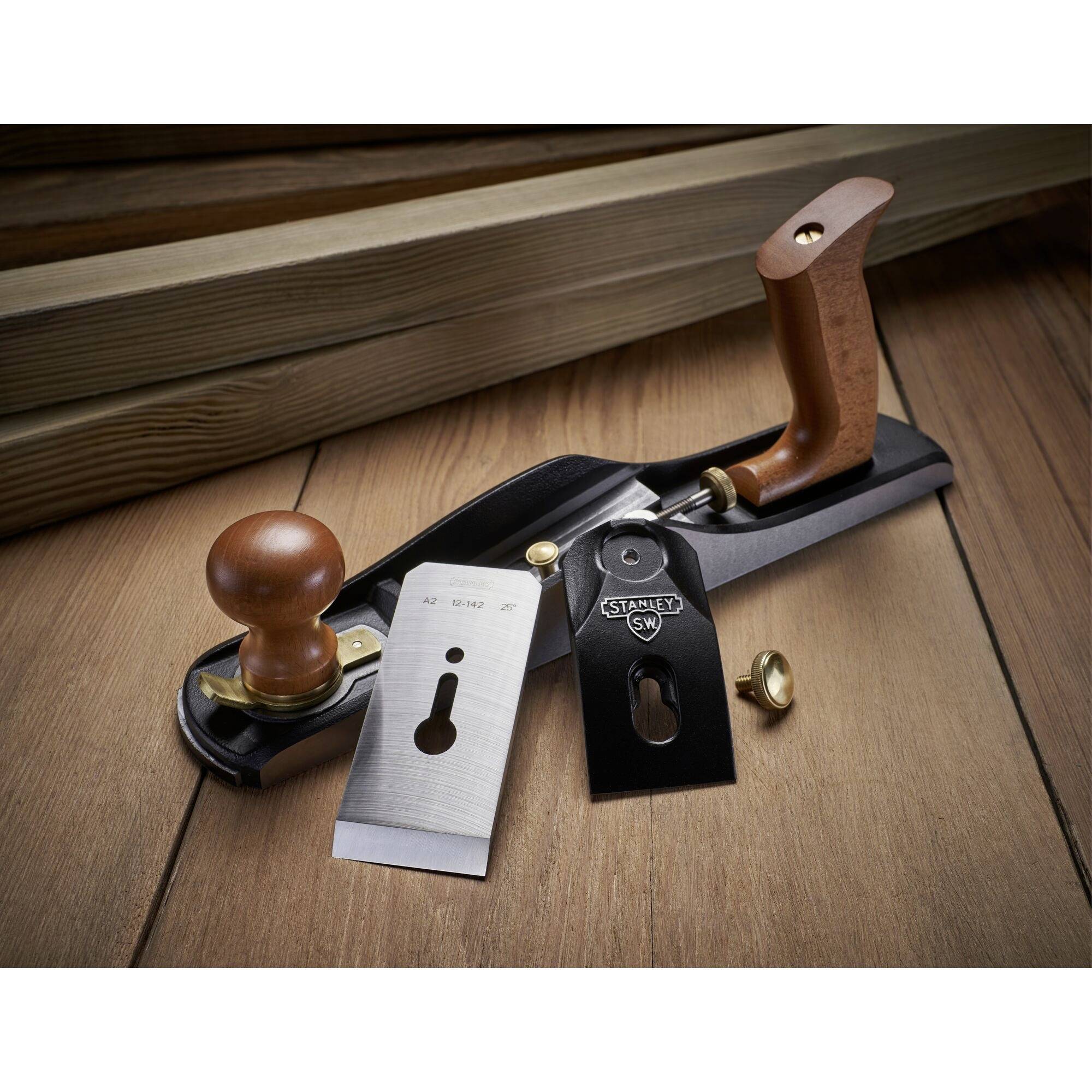 A wood plane with a wooden handle and adjustable blade is resting on a wooden surface. Wooden floorboards are visible in the background.
