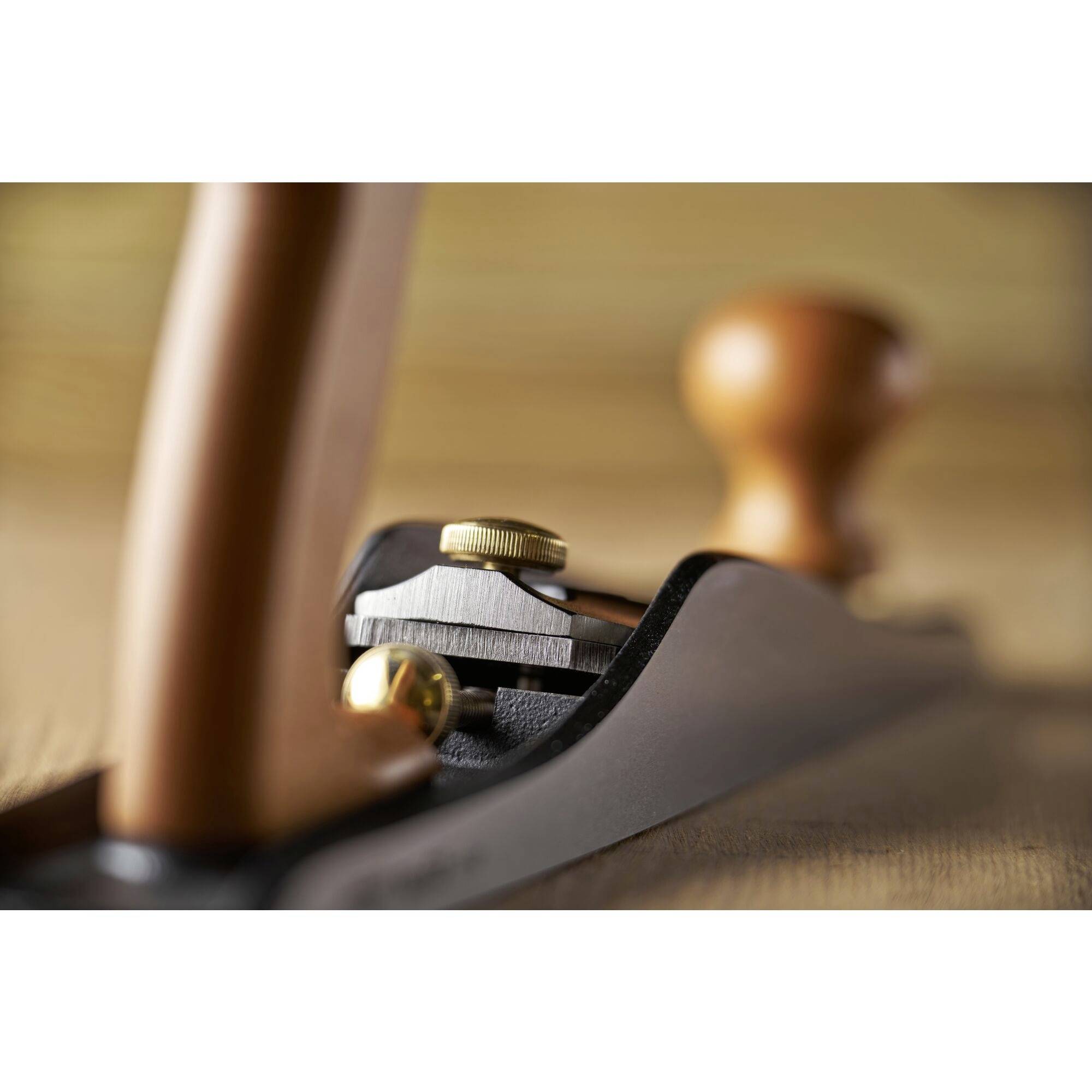 Metal hand plane with a wood-coloured handle, photographed in close-up on a workbench. The image captures precise craftsmanship.