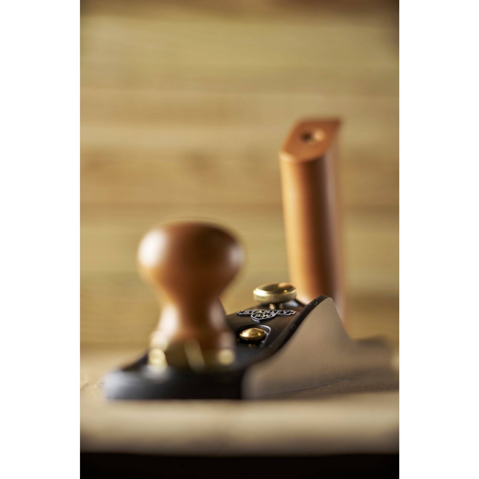 A wooden hand plane is in focus in the foreground, with a blurred background of wooden surfaces.