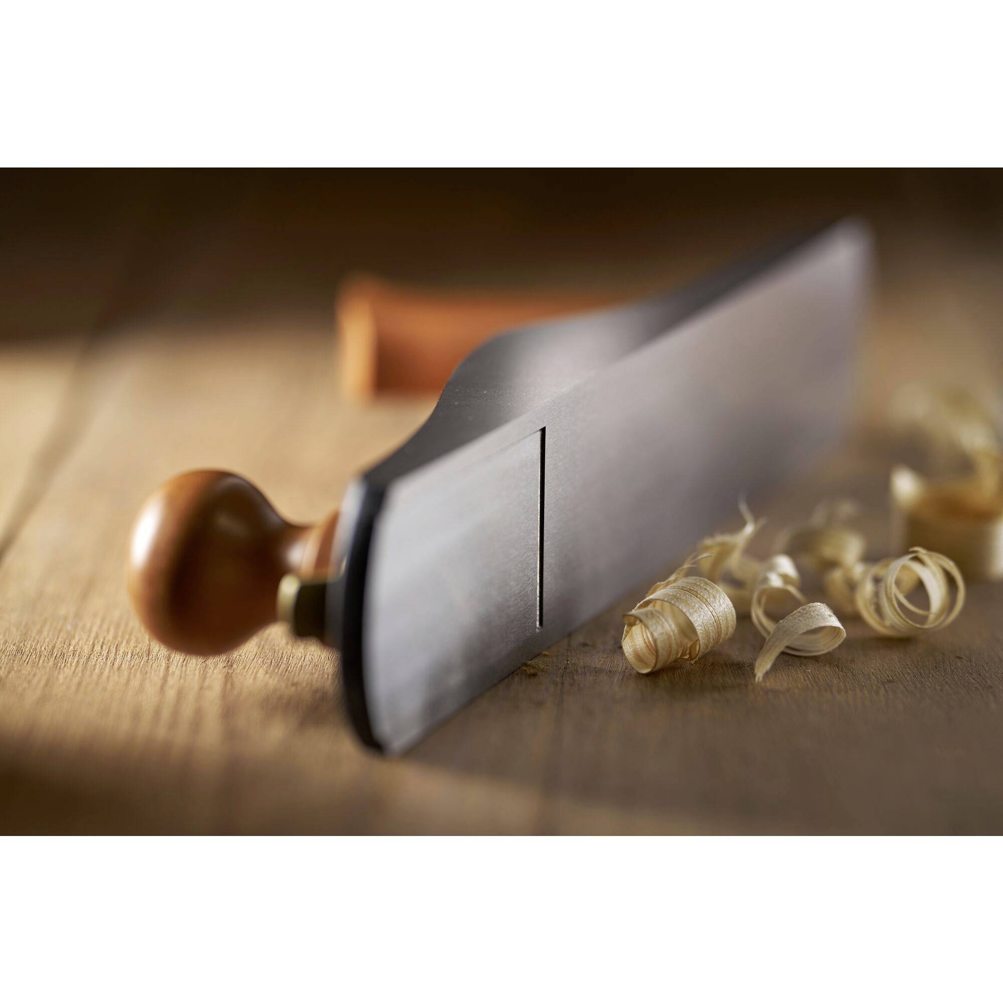 A wooden surface with a plane and wood shavings in view. The plane has a wooden handle and is blurred in the background.