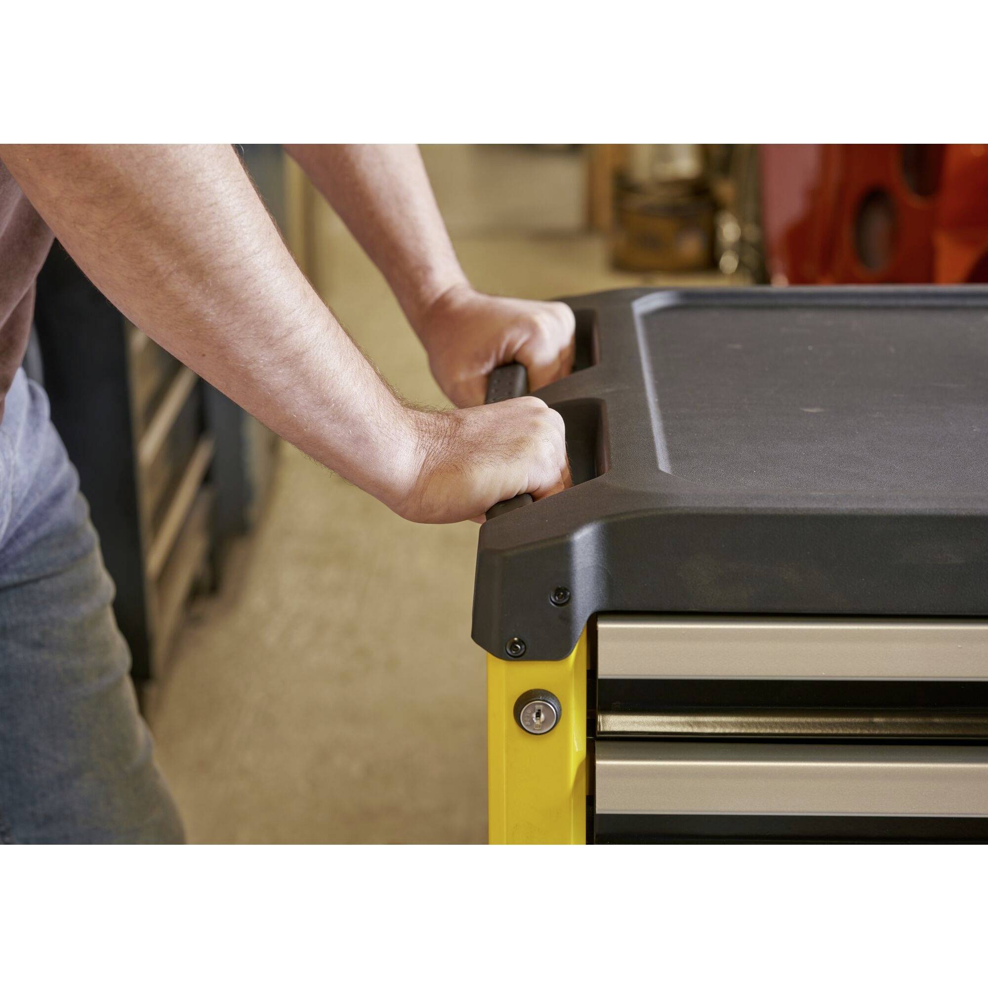 A person is leaning against a yellow toolbox with drawers, situated in a workshop environment.