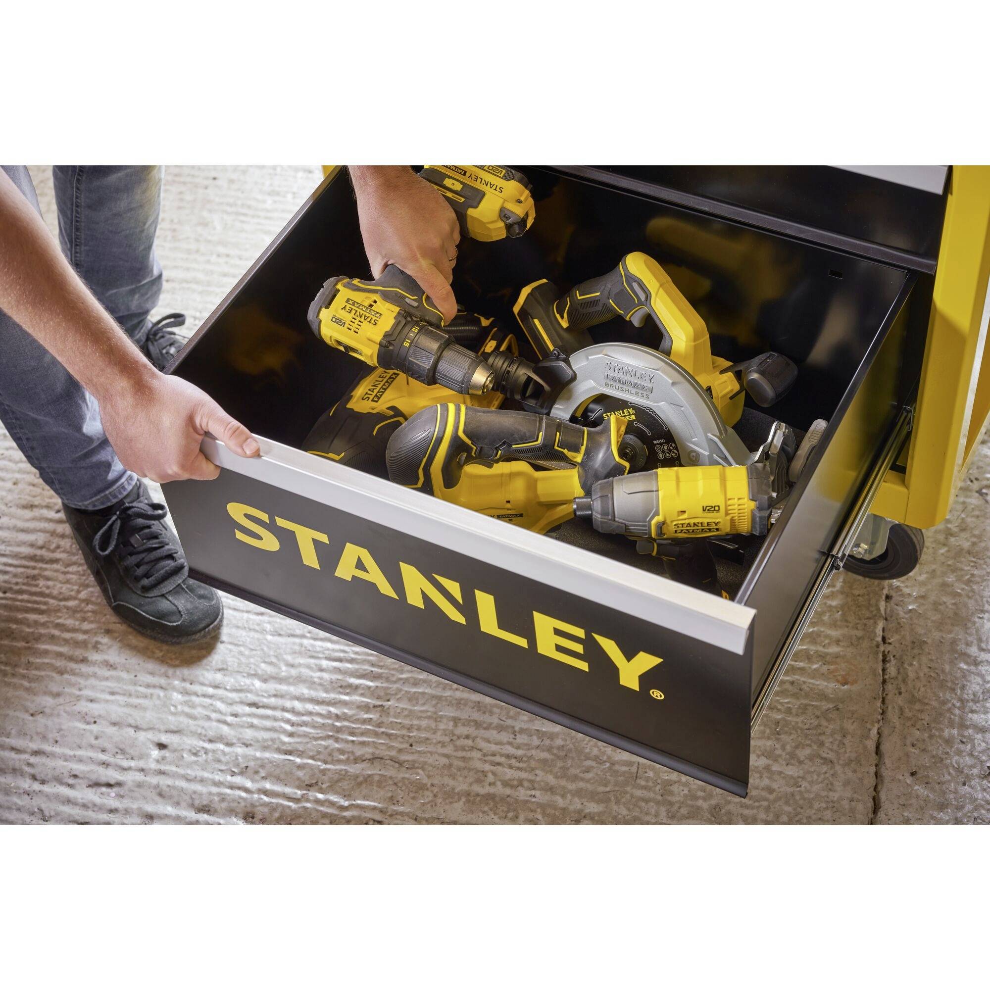 A person opens a drawer containing several yellow Stanley power tools, including a drill and a circular saw.