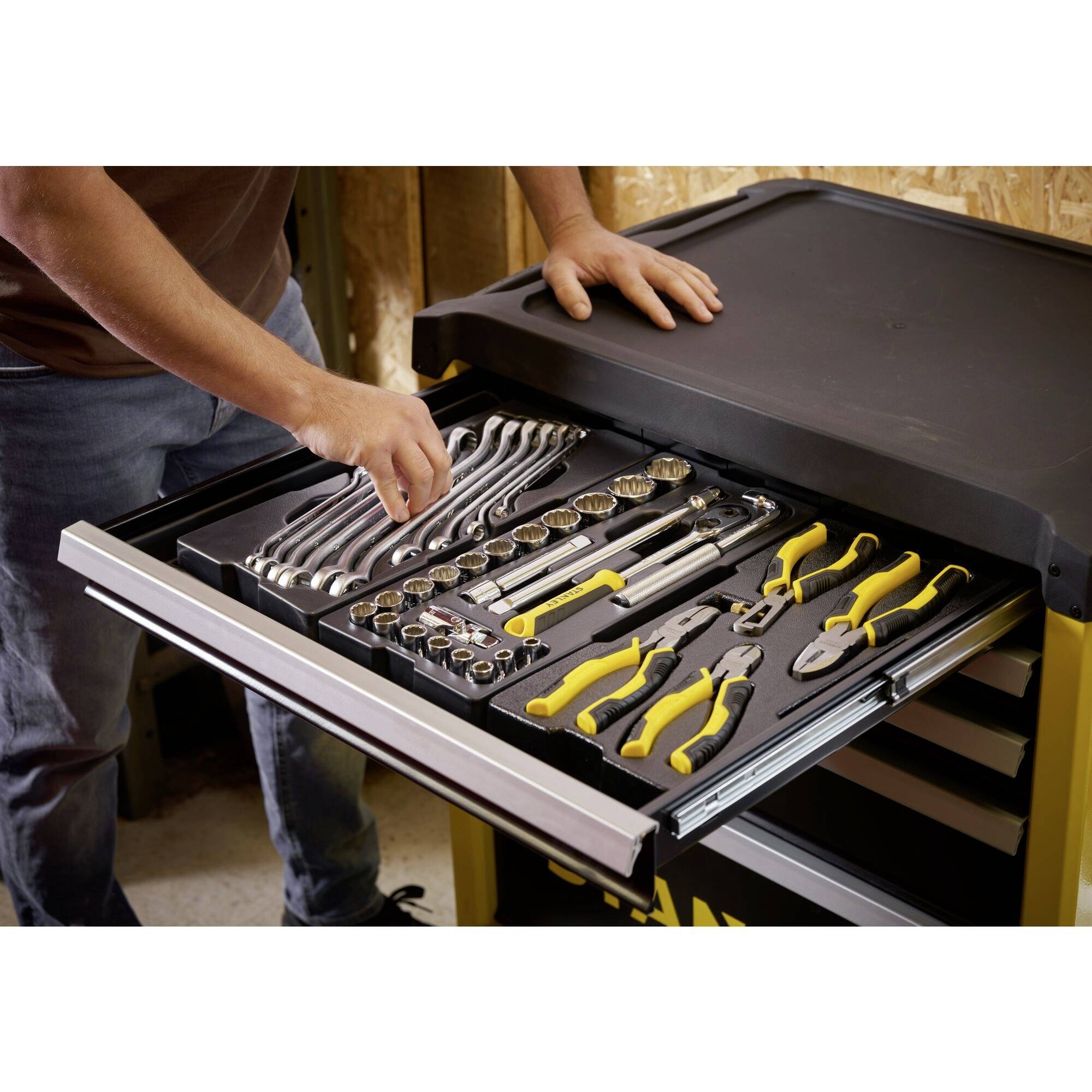 A man is arranging tools in a drawer of a tool trolley. Various hand tools such as spanners and pliers are visible.