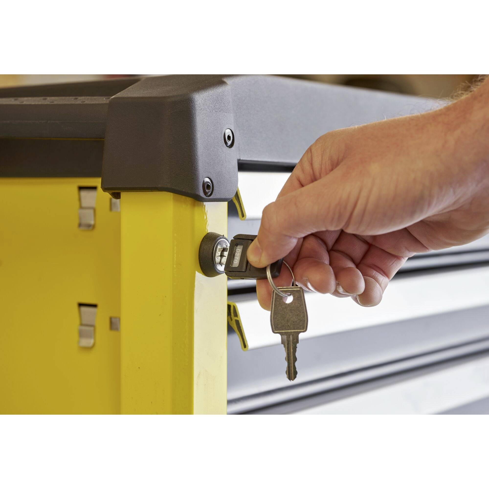 A hand inserts a key into the lock of a yellow tool cabinet.